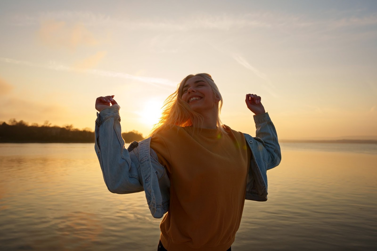 A woman by the sea smiling with two hands slightly raised