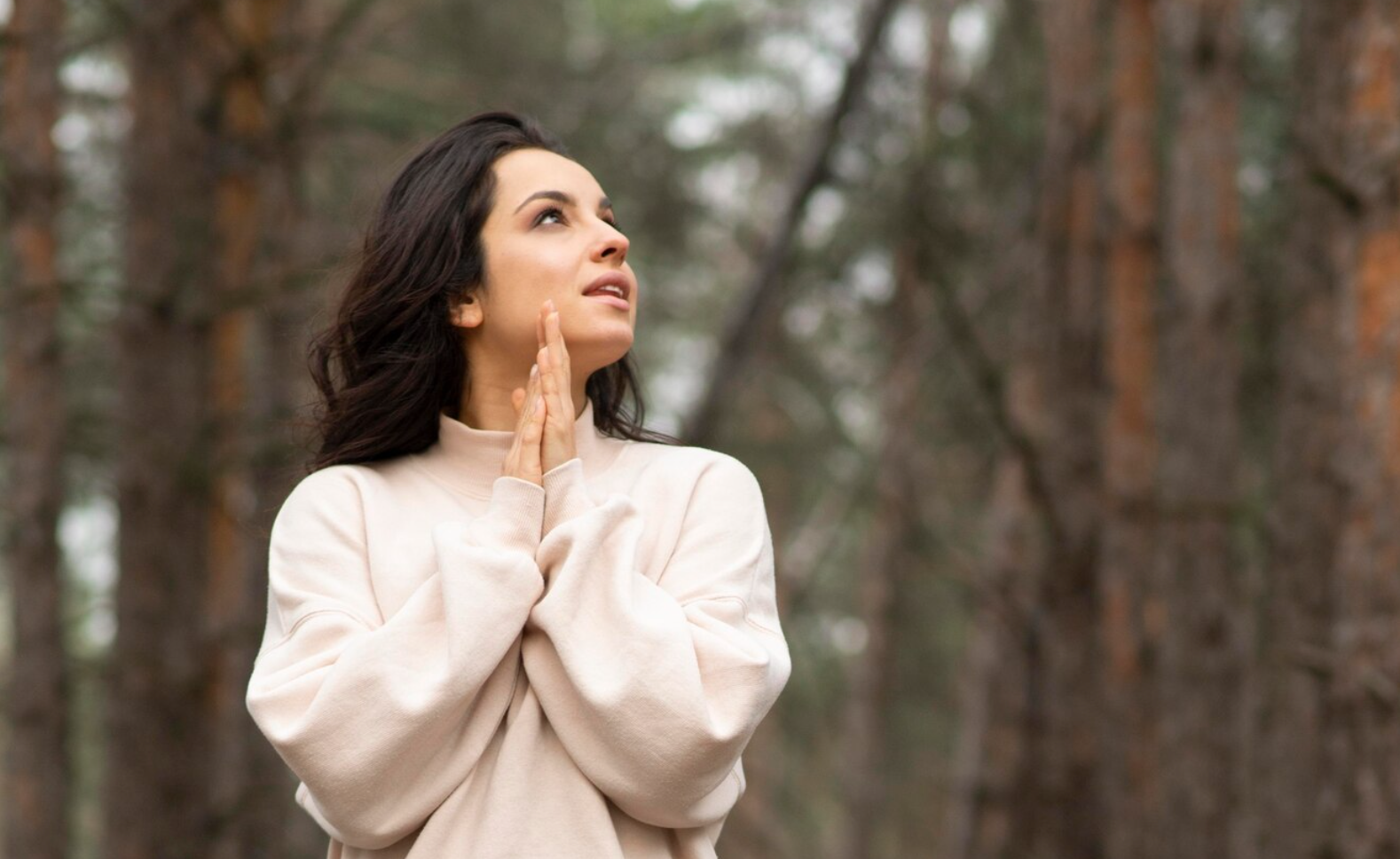 A woman shot in a low angle in a forest, holding her hands together and enjoying the cognitive benefits of ketamine therapy