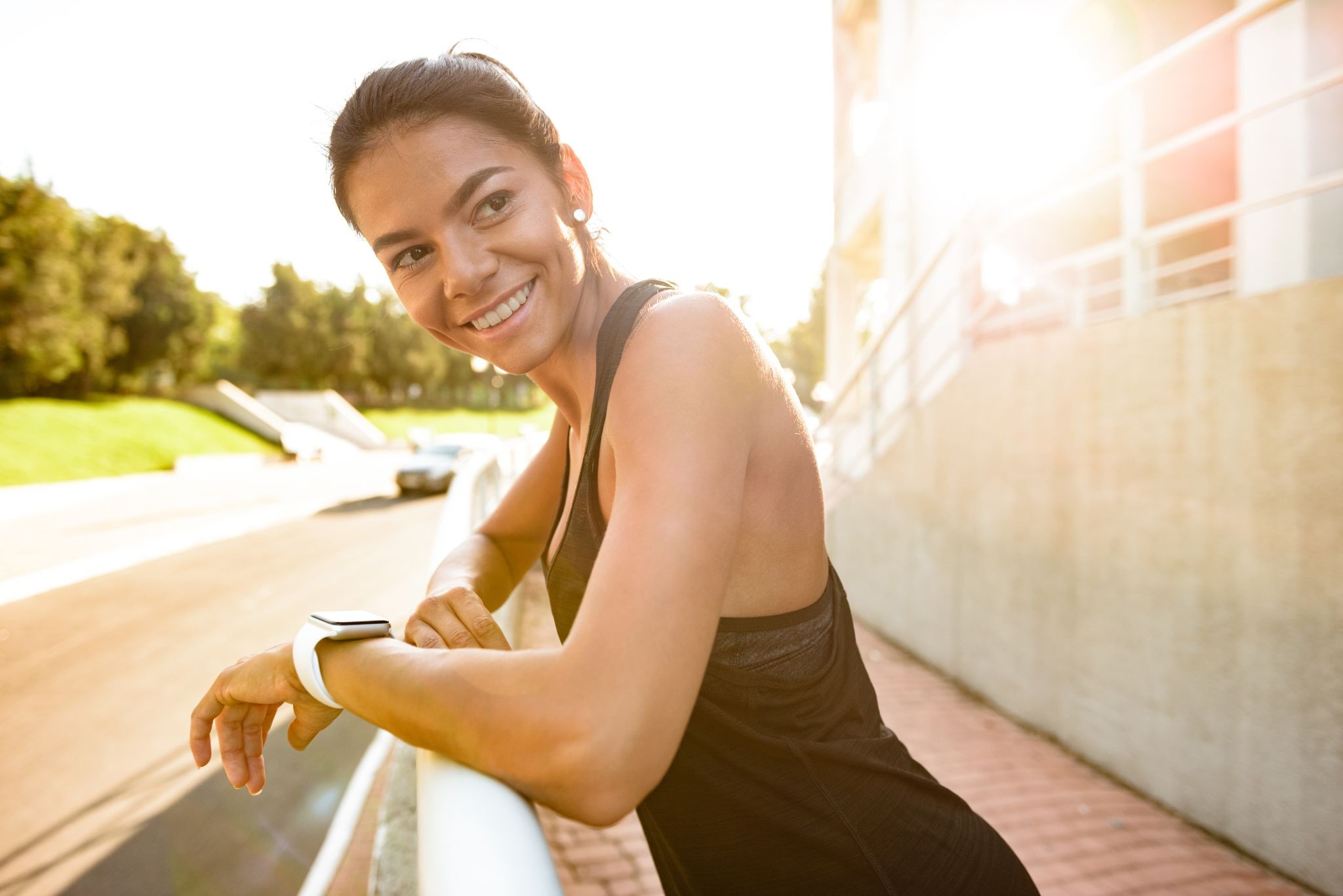 A fit woman standing by a railing in a park, smiling and enjoying the benefits of going to a Utah wellness clinic