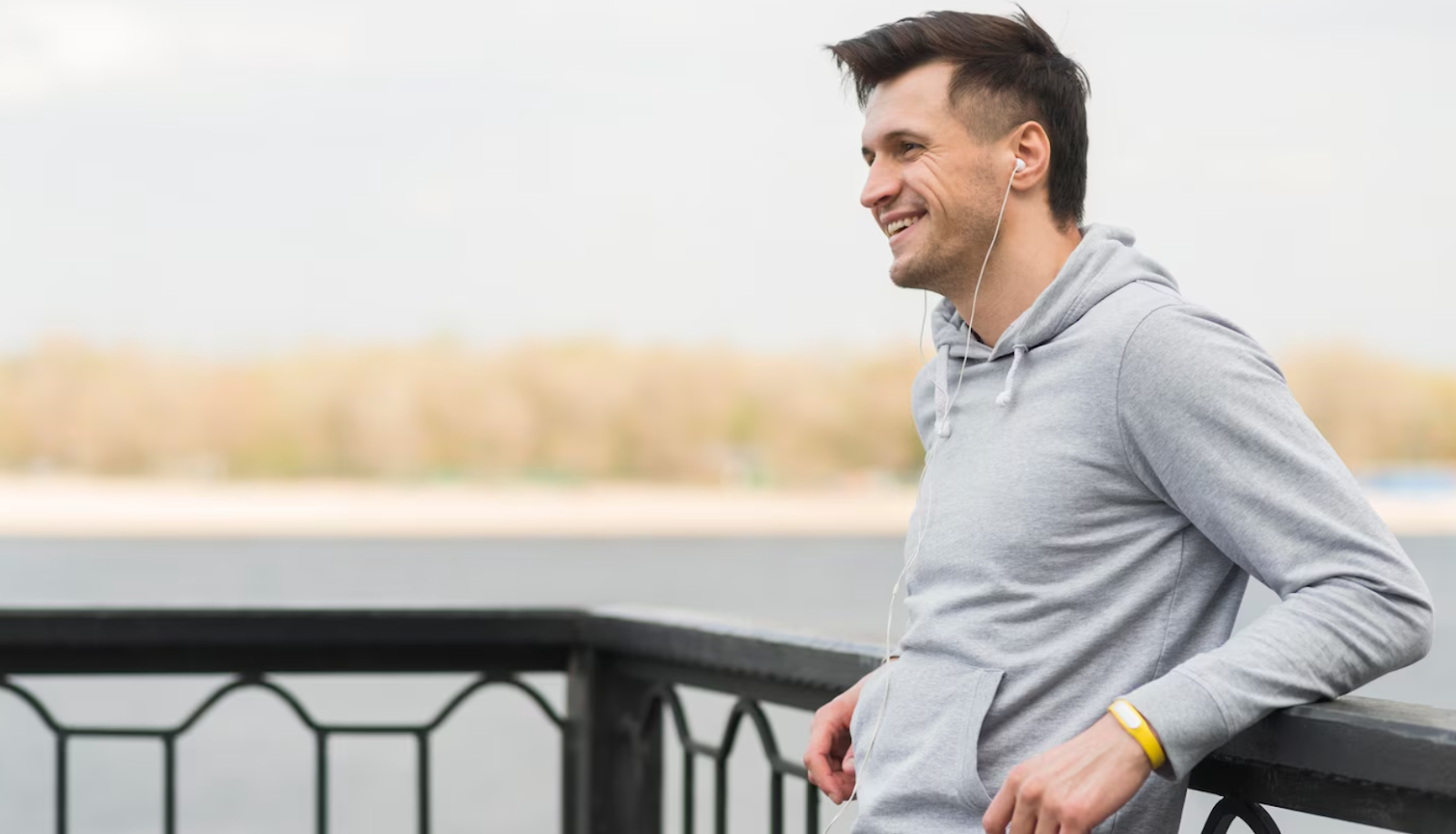 A man wearing earphones, standing by a park railing, and enjoying the benefits of testosterone therapy