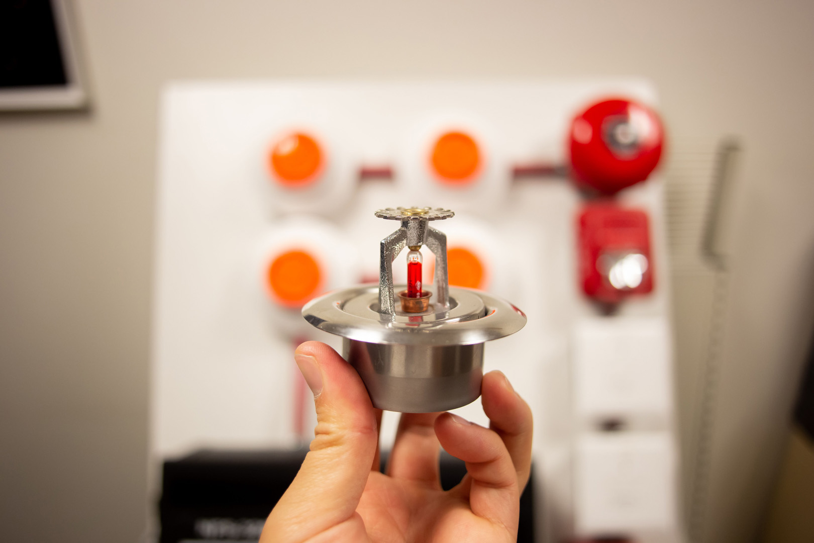 Hand holding a silver fire alarm system sensor during installation
