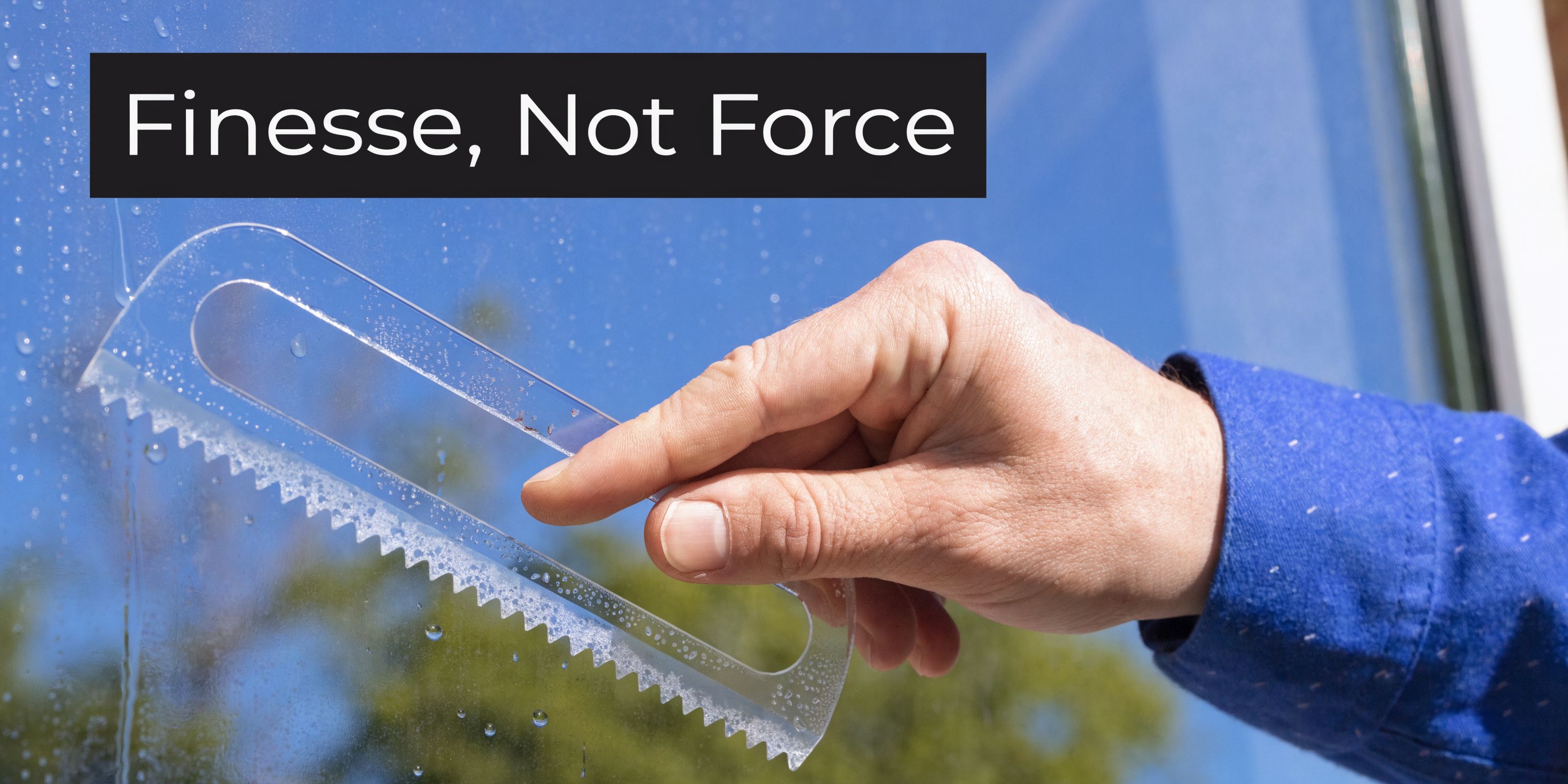 A hand using a specialized plastic scraper tool to gently clean water droplets off a glass window.