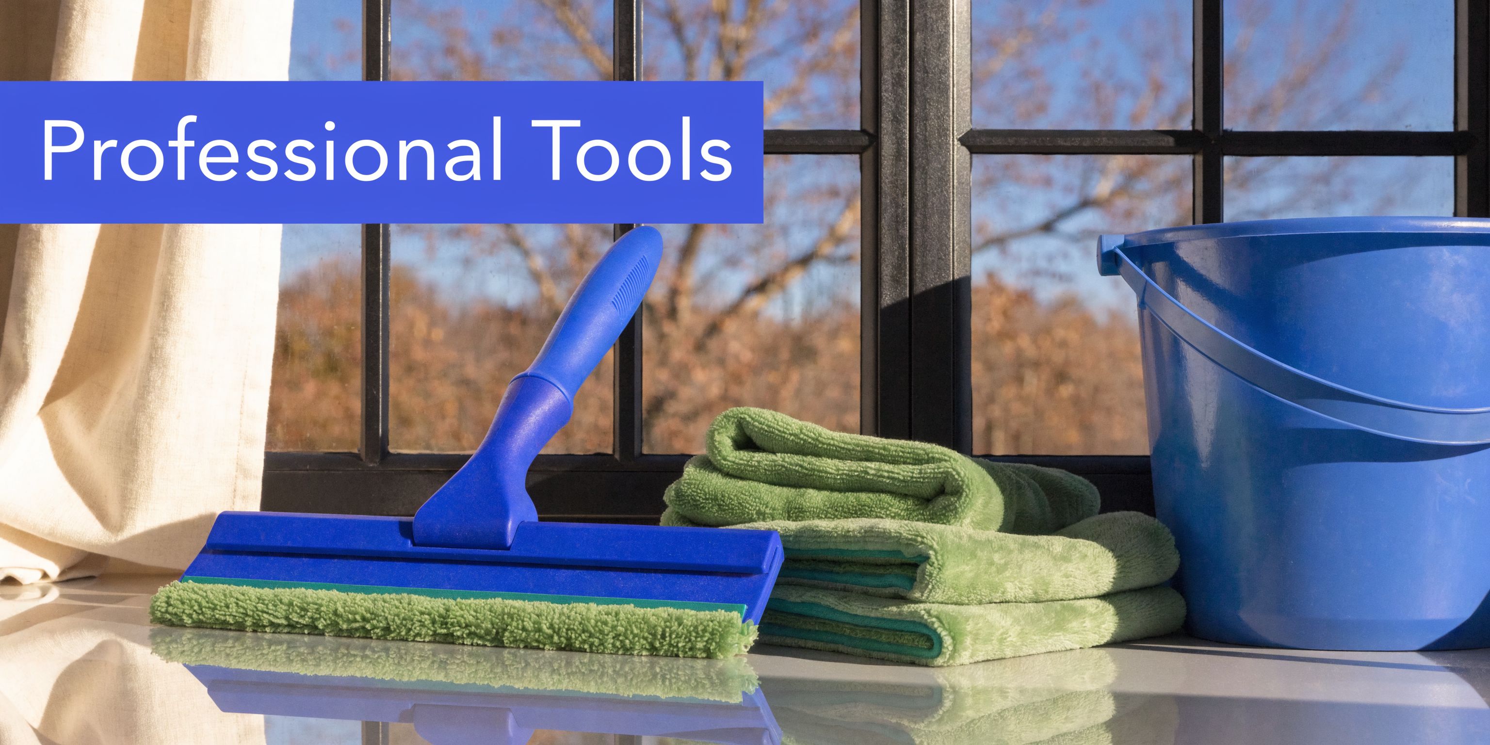 A professional window cleaning squeegee, green microfiber cloths, and a blue plastic bucket on a windowsill.