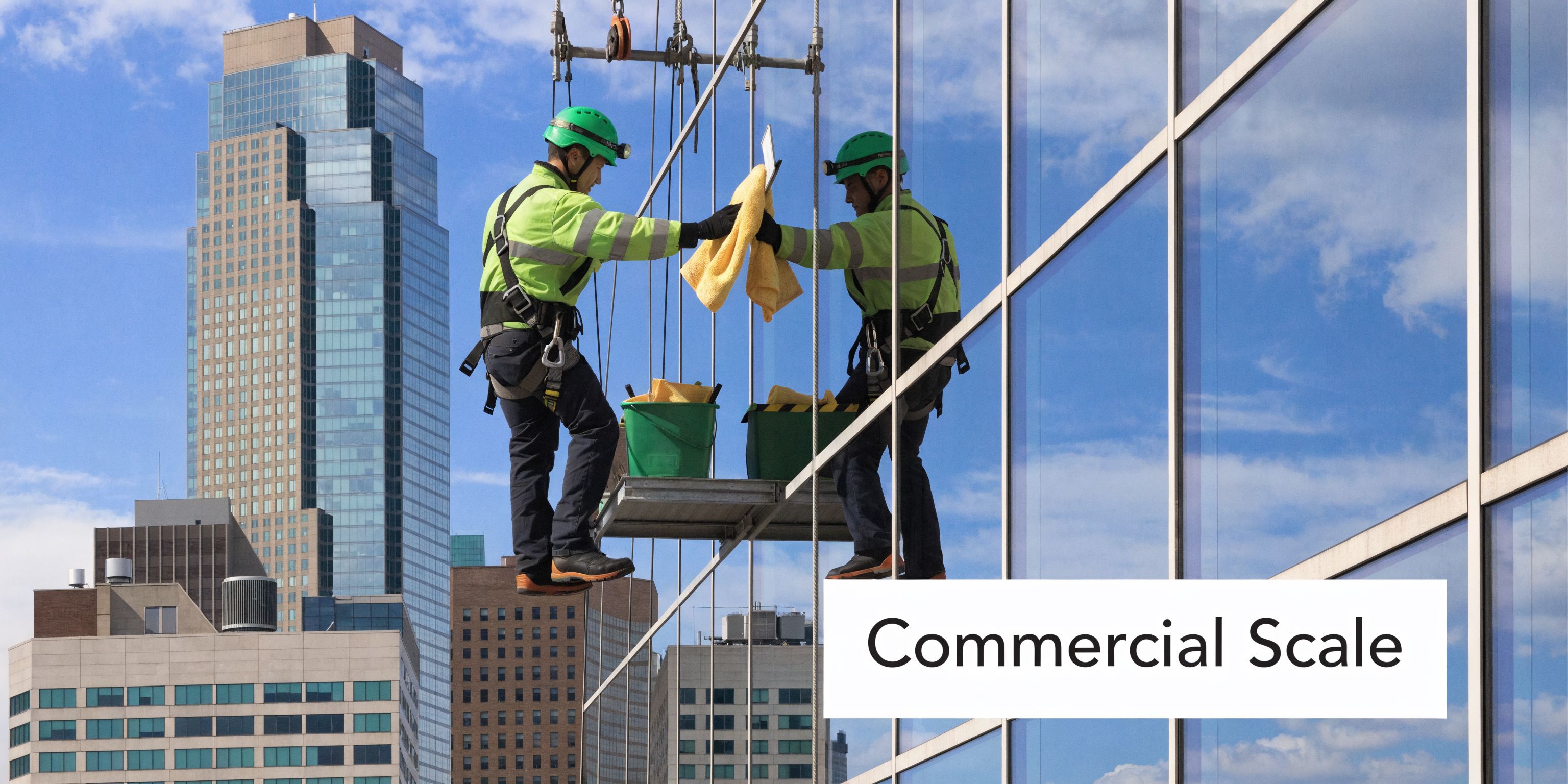 Two window cleaners working on a platform while cleaning glass panels of a high-rise city skyscraper.