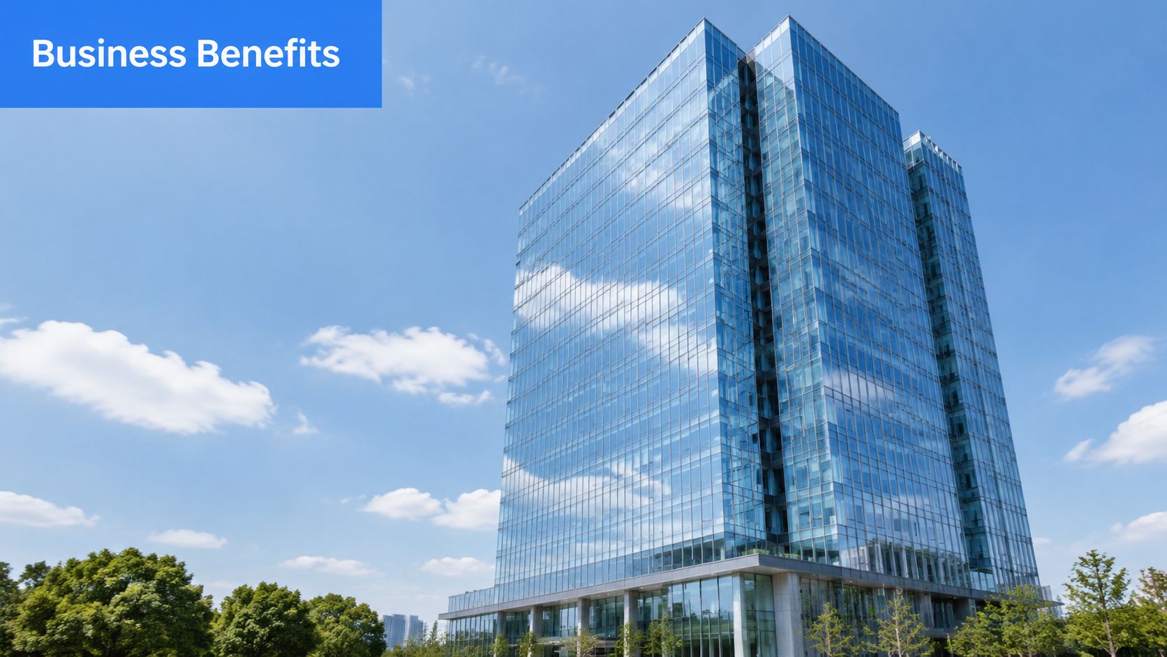 A tall modern skyscraper with a glass facade reflecting blue skies and clouds above green trees.