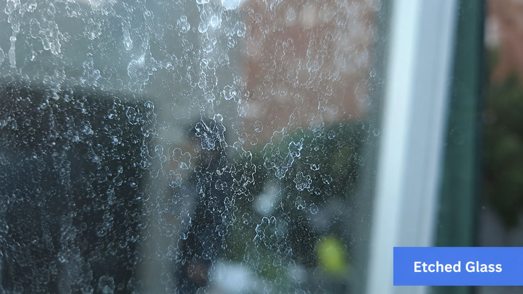 Close-up of a glass window covered in heavy white mineral deposits caused by hard water spots.