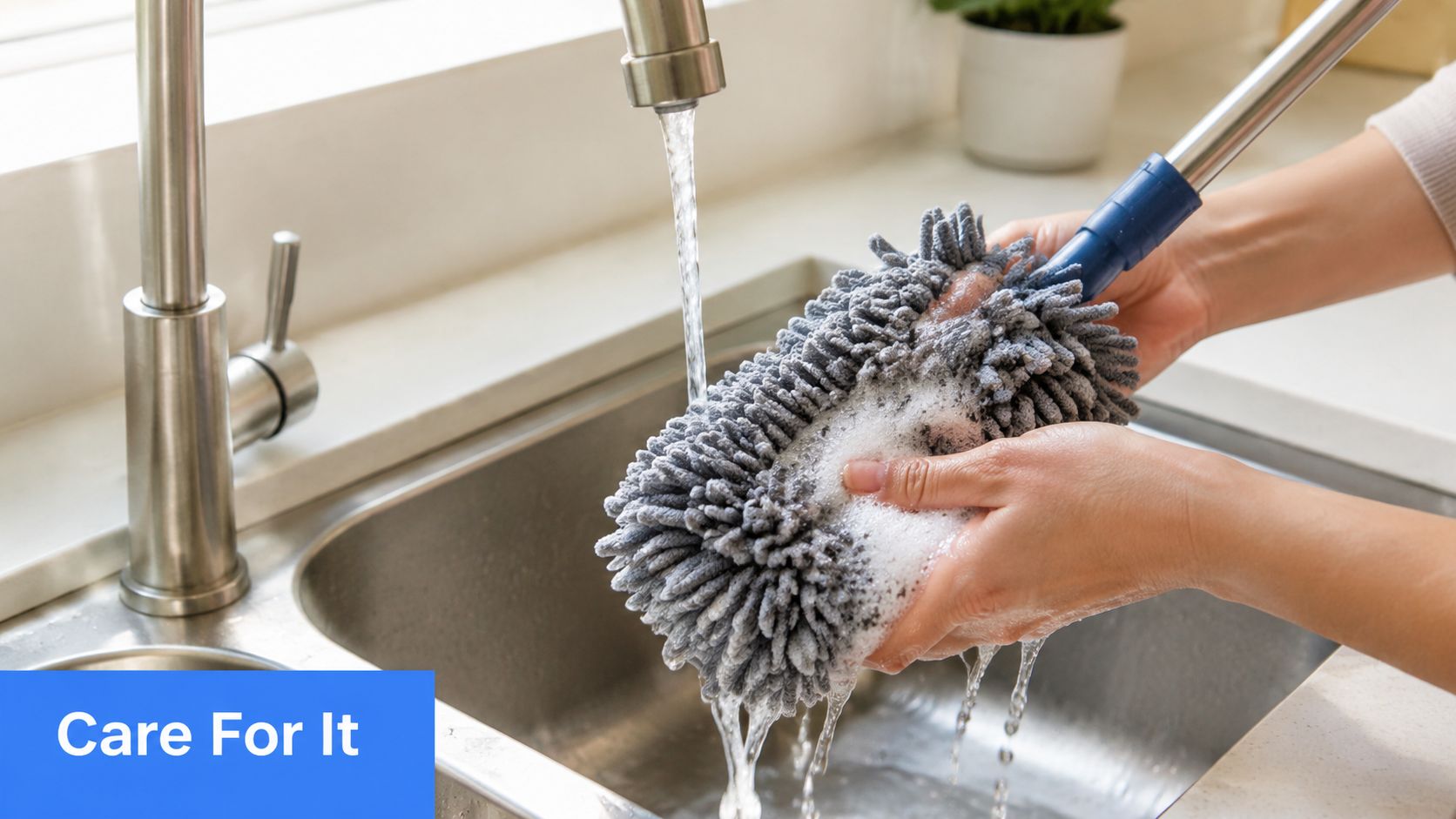 A person washing a grey microfiber duster head under a kitchen faucet with soapy water and bubbles.