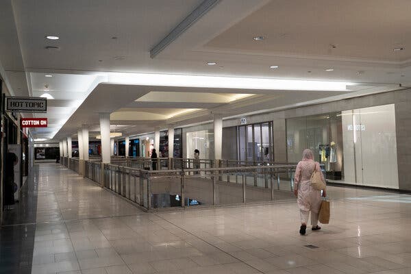 A woman facing away from the camera walks in a mostly empty shopping mall.