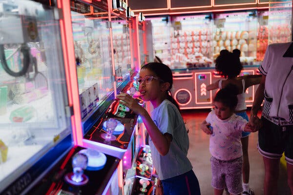 A child plays a claw machine game in a neon-lit arcade.