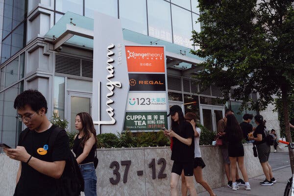 People walk past signs for a shopping mall on a city street.
