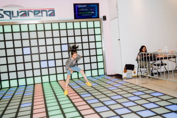 A young girl jumps on colorful lighted square tiles in an interactive floor game.