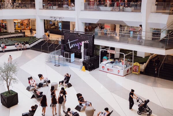 People sit on chairs and walk around an atrium in a shopping mall.