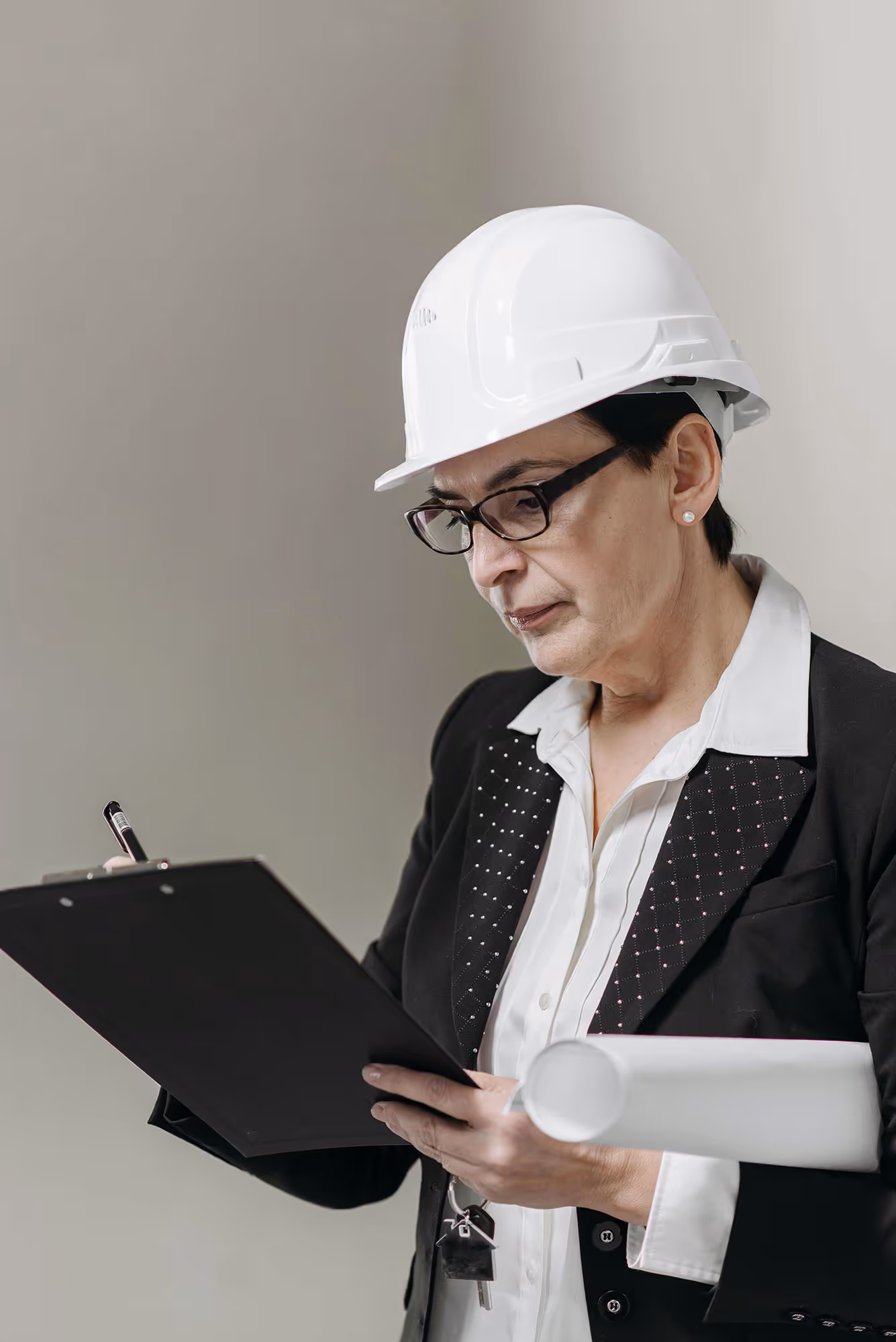 Female architect or construction project manager wearing a white hard hat and black blazer, reviewing documents on a clipboard while holding rolled-up blueprints. The image highlights women in engineering, architecture, and leadership roles within construction and infrastructure development.