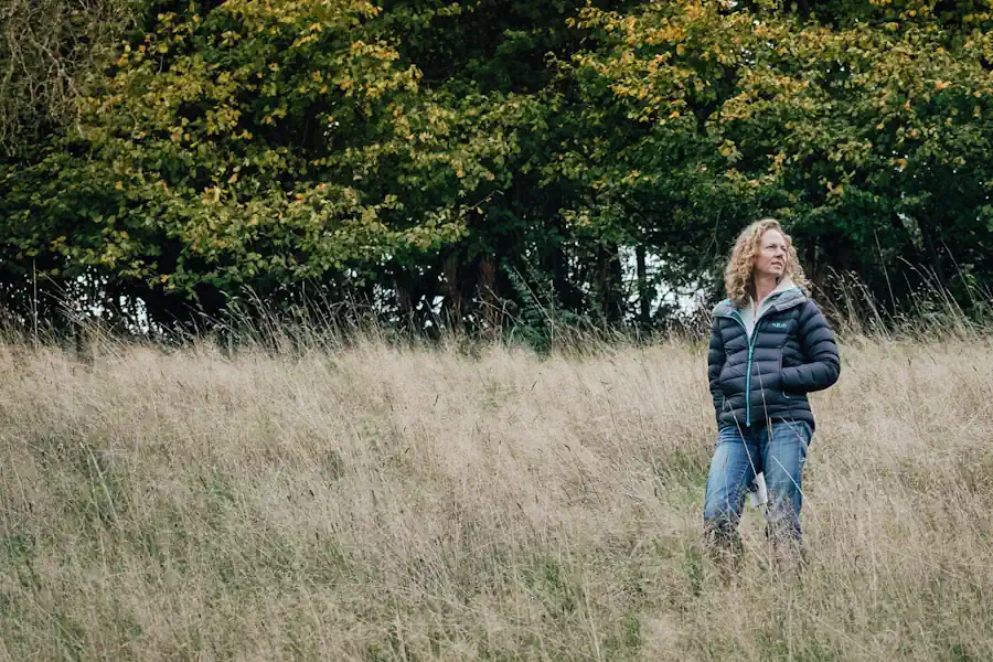Woman standing in long grassland in front of woodland