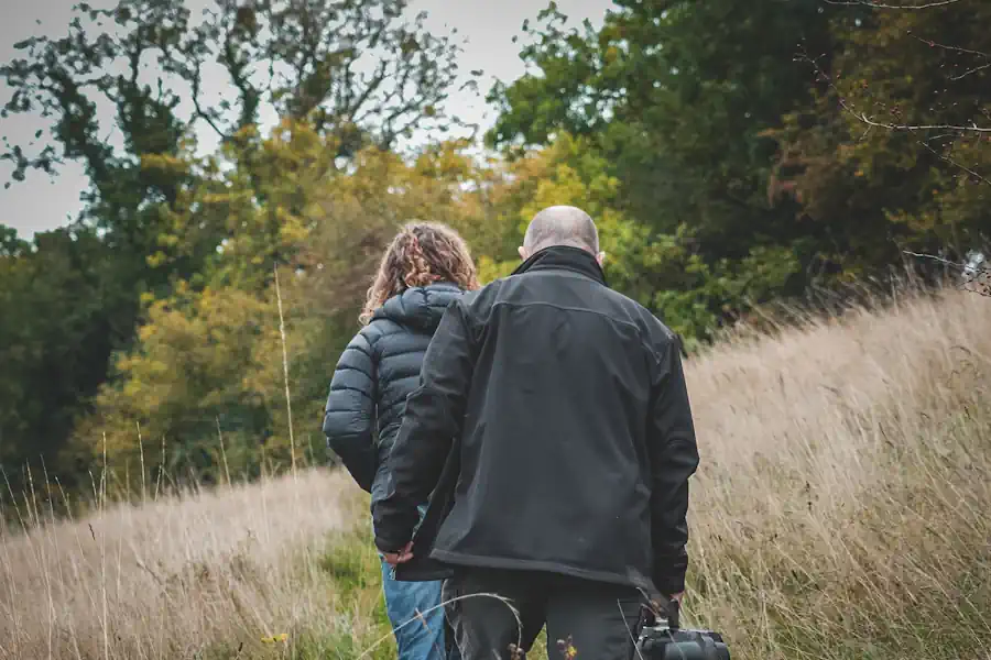 Two people walking through grassland towards woodland