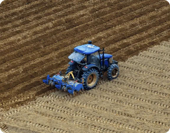 Blue tractor plowing a field with furrows in rows.