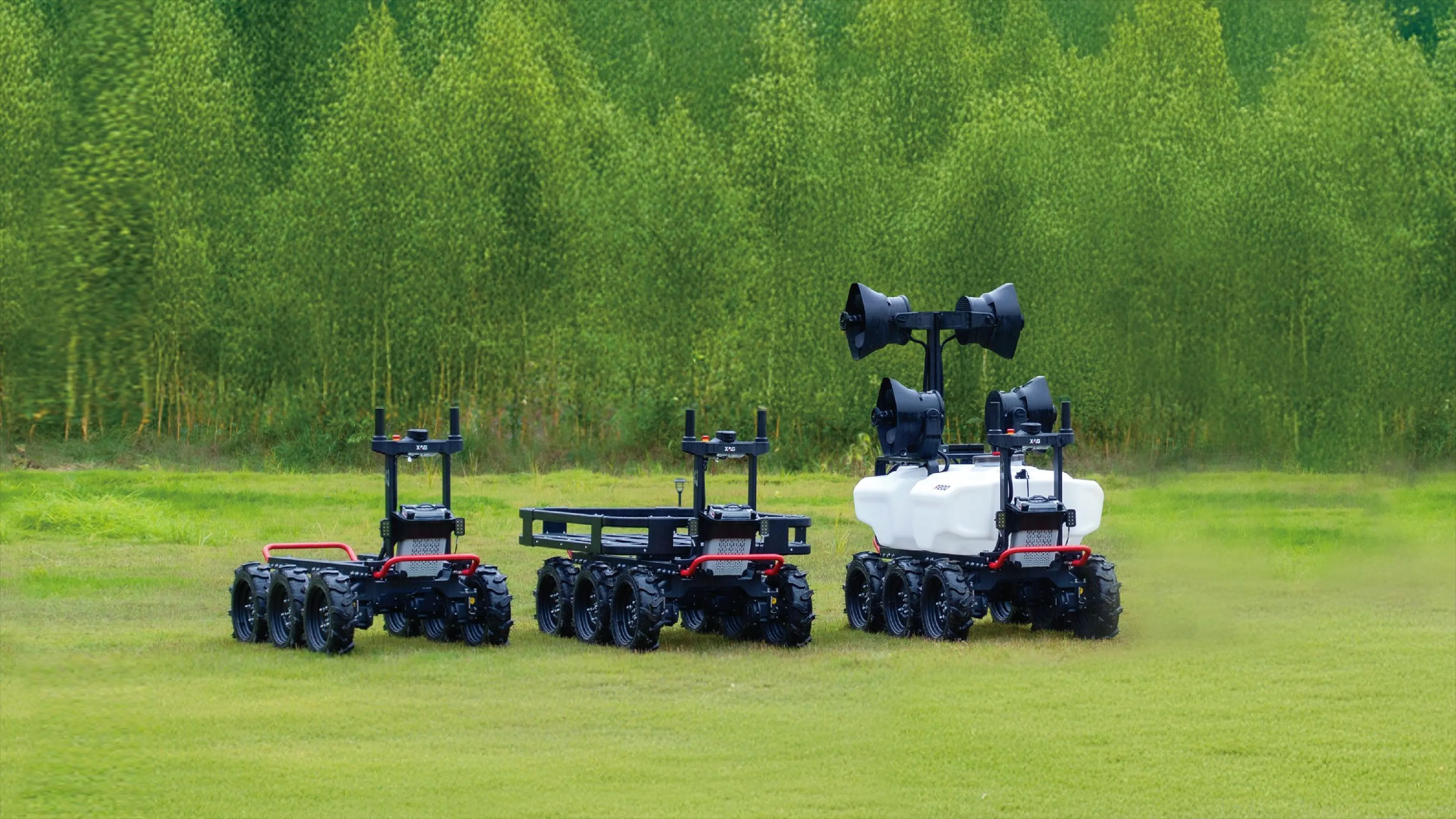 Three black all-terrain robots with six wheels on green grass with forest background