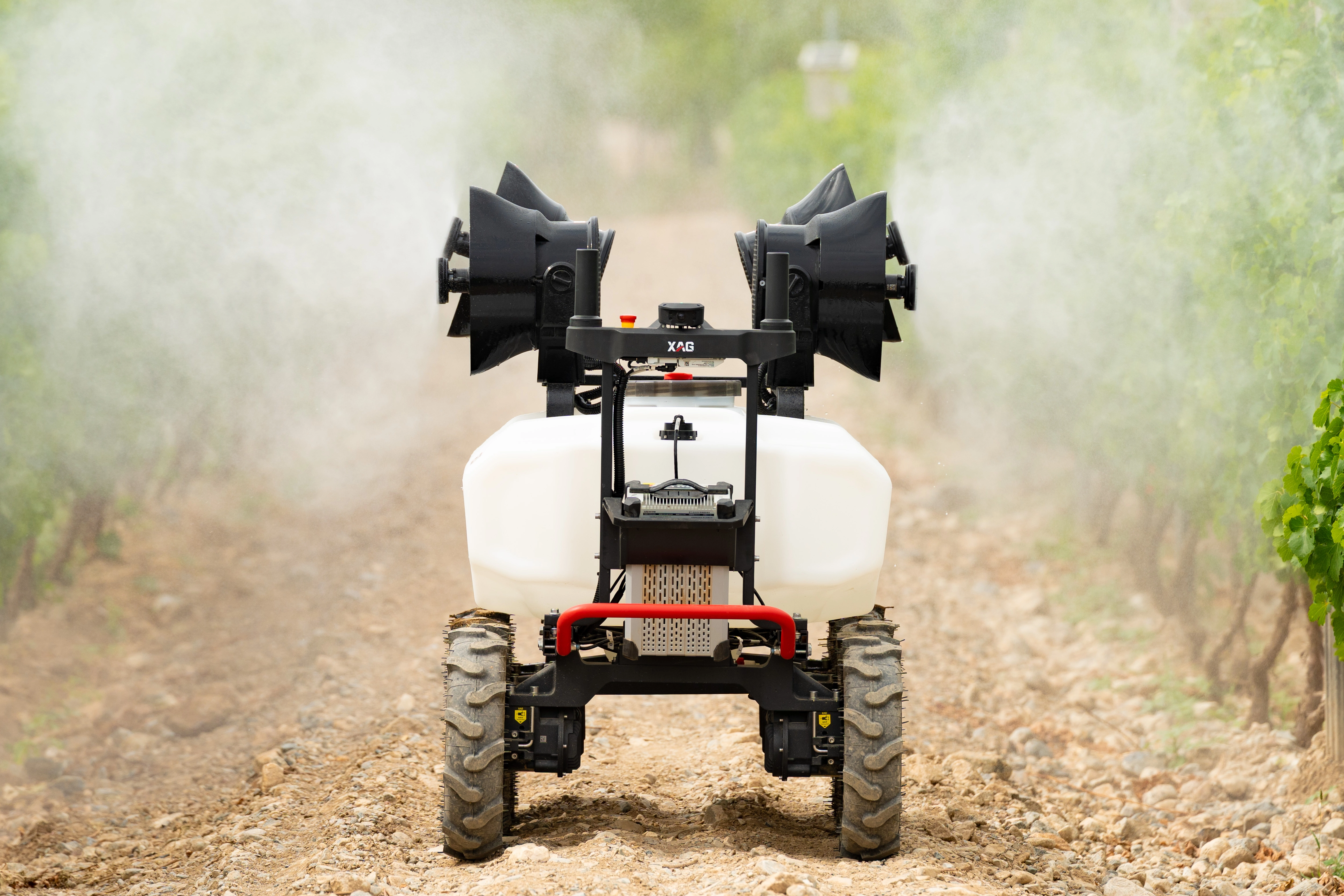 Autonomous agricultural robot spraying mist between rows of crops on a dirt path