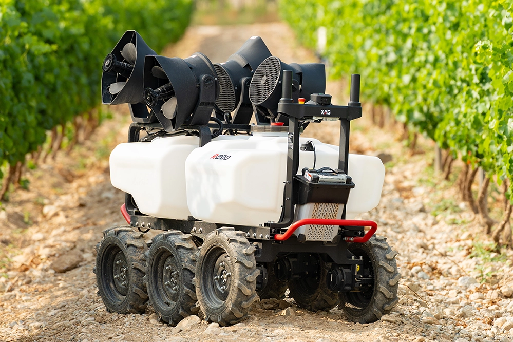 Six-wheeled agricultural robot with white tanks and black equipment on grassy field