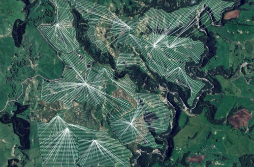 Drone spraying water mist over a netted agricultural field under sunlight.
