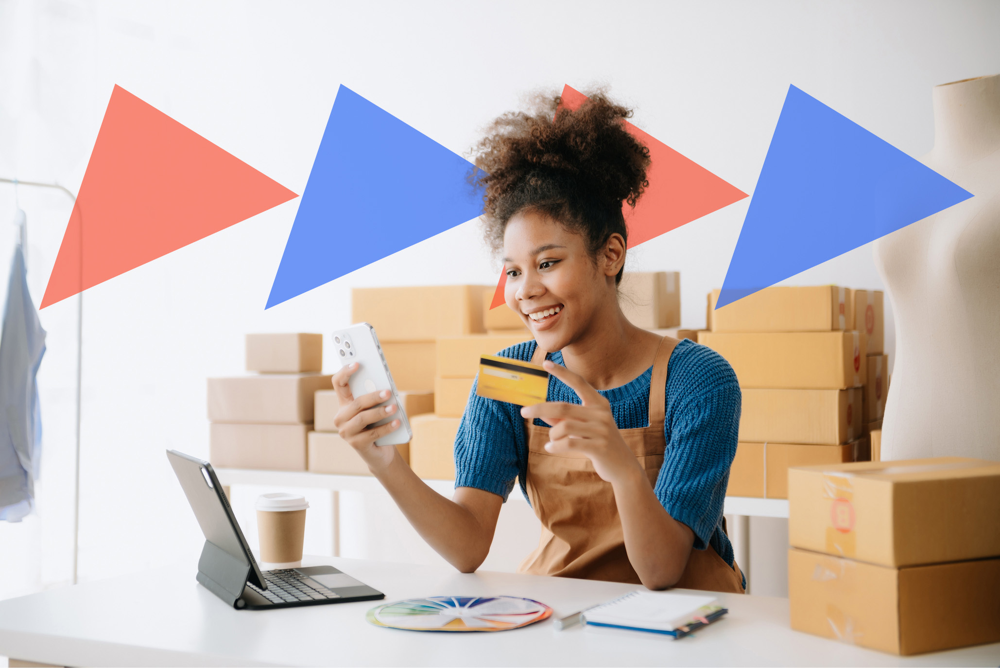 Small business owner holding credit card and phone while fulfilling online orders in a creative studio workspace.