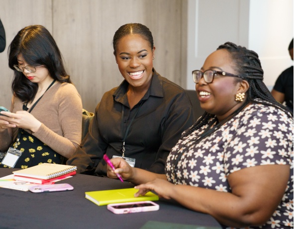 Two women smiling while another looks at her phone