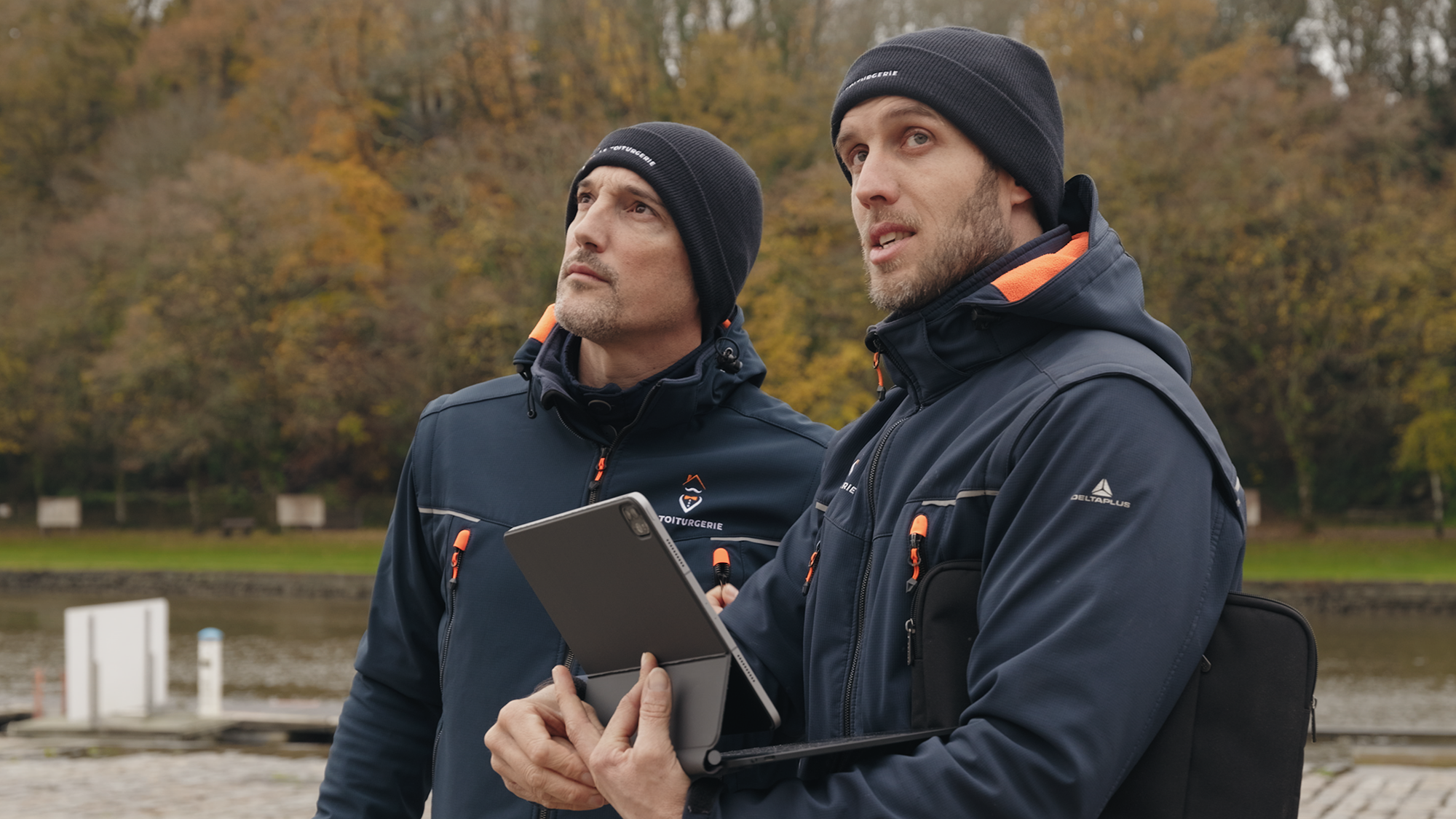 Toituriers en vestes bleues et bonnets regardant en l'air avec une tablette.