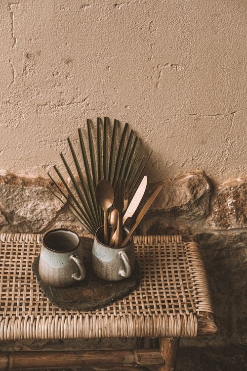 Two cups are on a table with a wicker basket and a spoon.