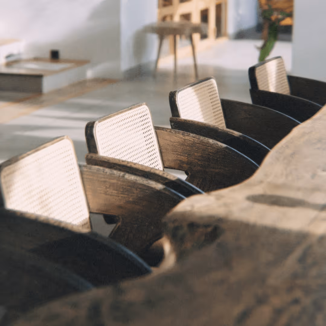 Vier braune Holzstühle mit weißen Geflechtlehnen an einem großen Holztisch.