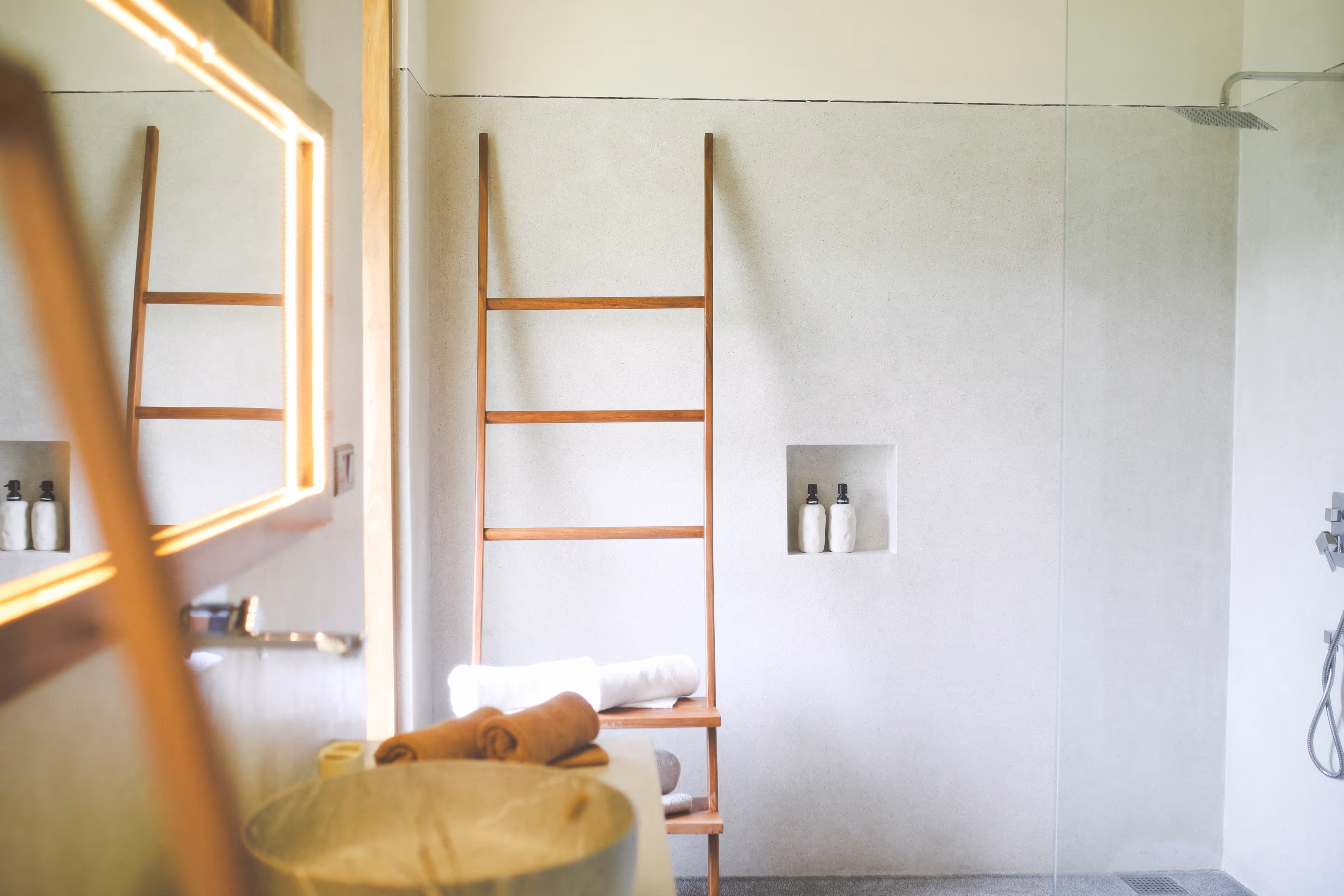 Modernes Badezimmer mit Holzleiter, Handtüchern und begehbarer Dusche mit Regendusche.