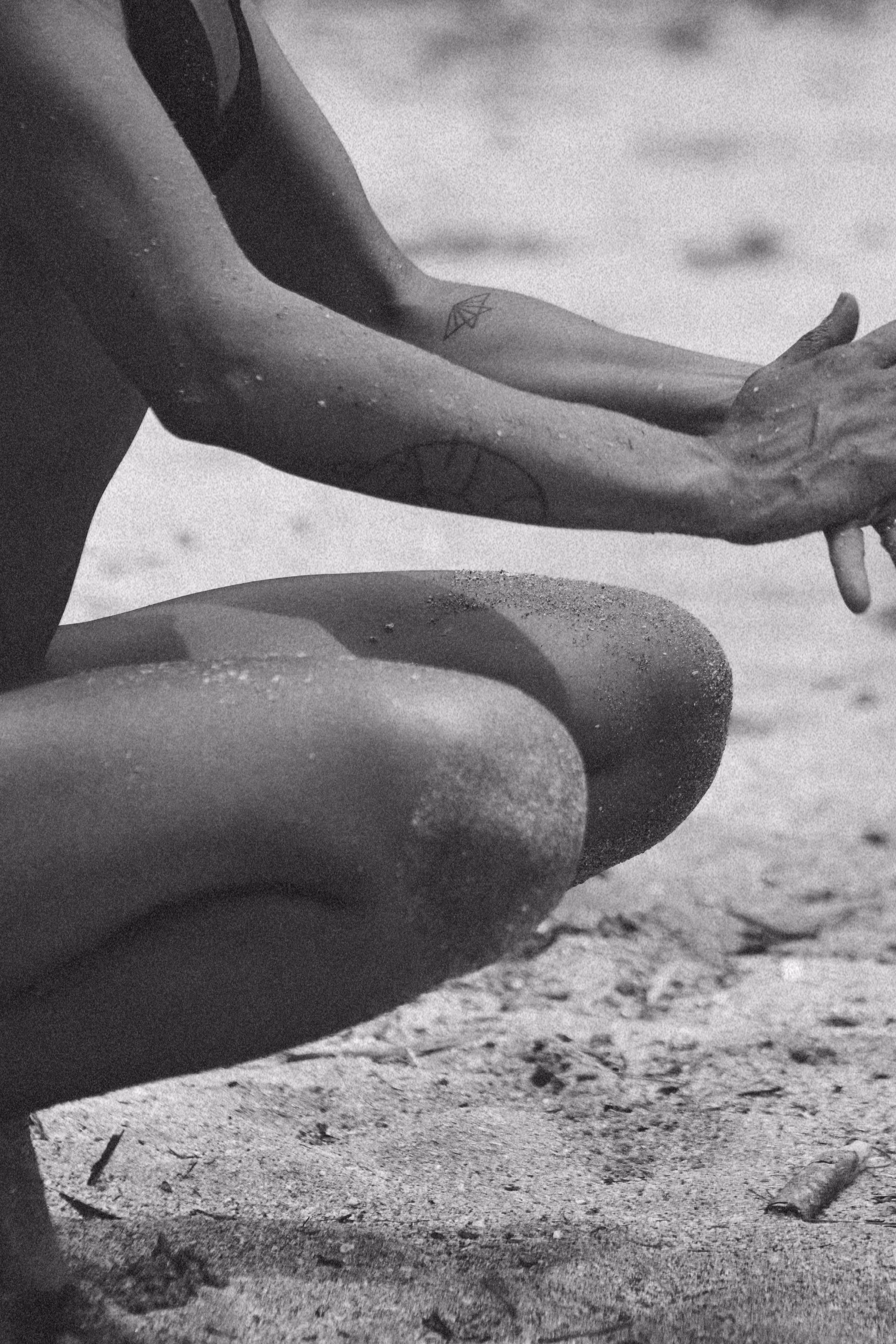 Nasse Arme und Beine mit Sand bedeckt sitzen am Strand im schwarzen Badeanzug.