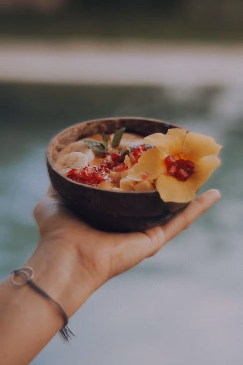 Hand hält eine Schale mit Smoothie, garniert mit roten Früchten und einer gelben Blüte.