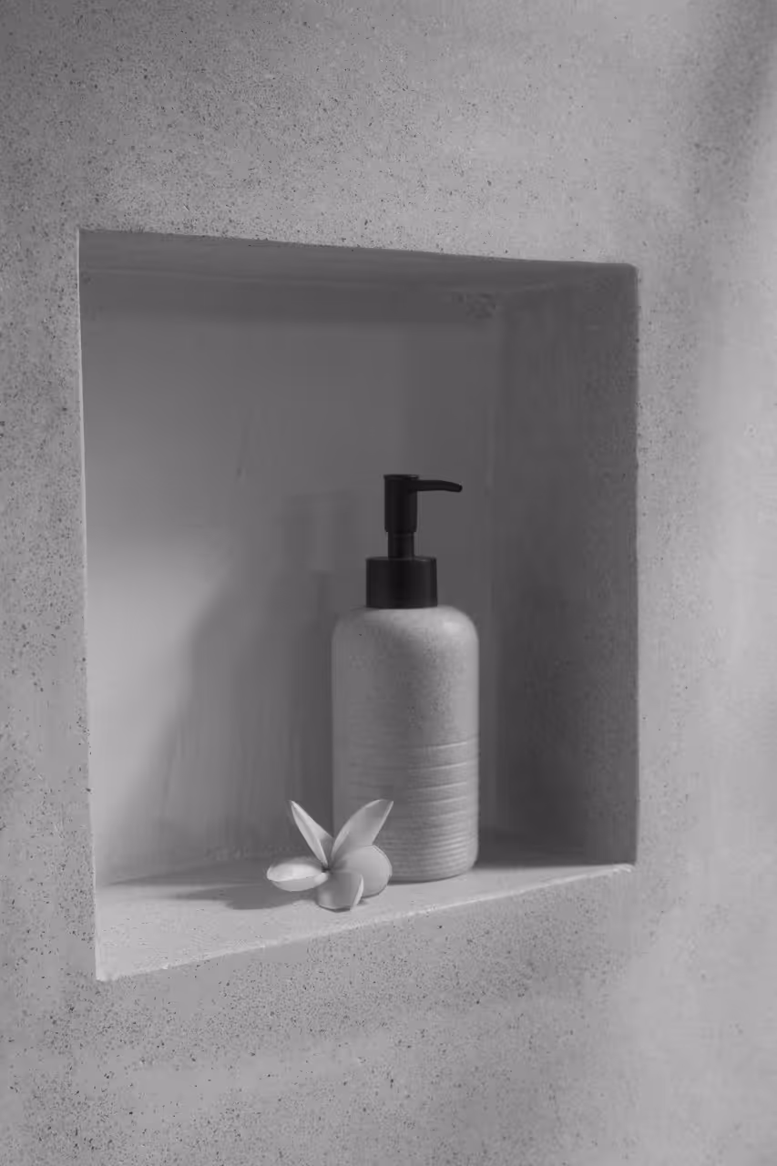 Flaschenpumpe und Blume auf eingebautem Regal in einer Betonwand.