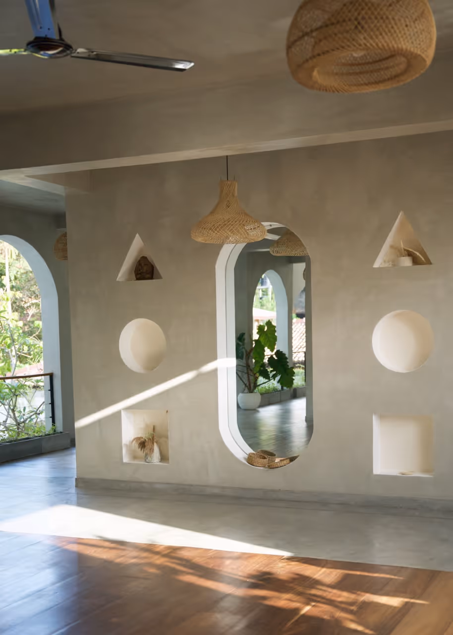 Minimalist room with arched windows, geometric wall niches, hanging wicker lamps, and sunlight on floor.