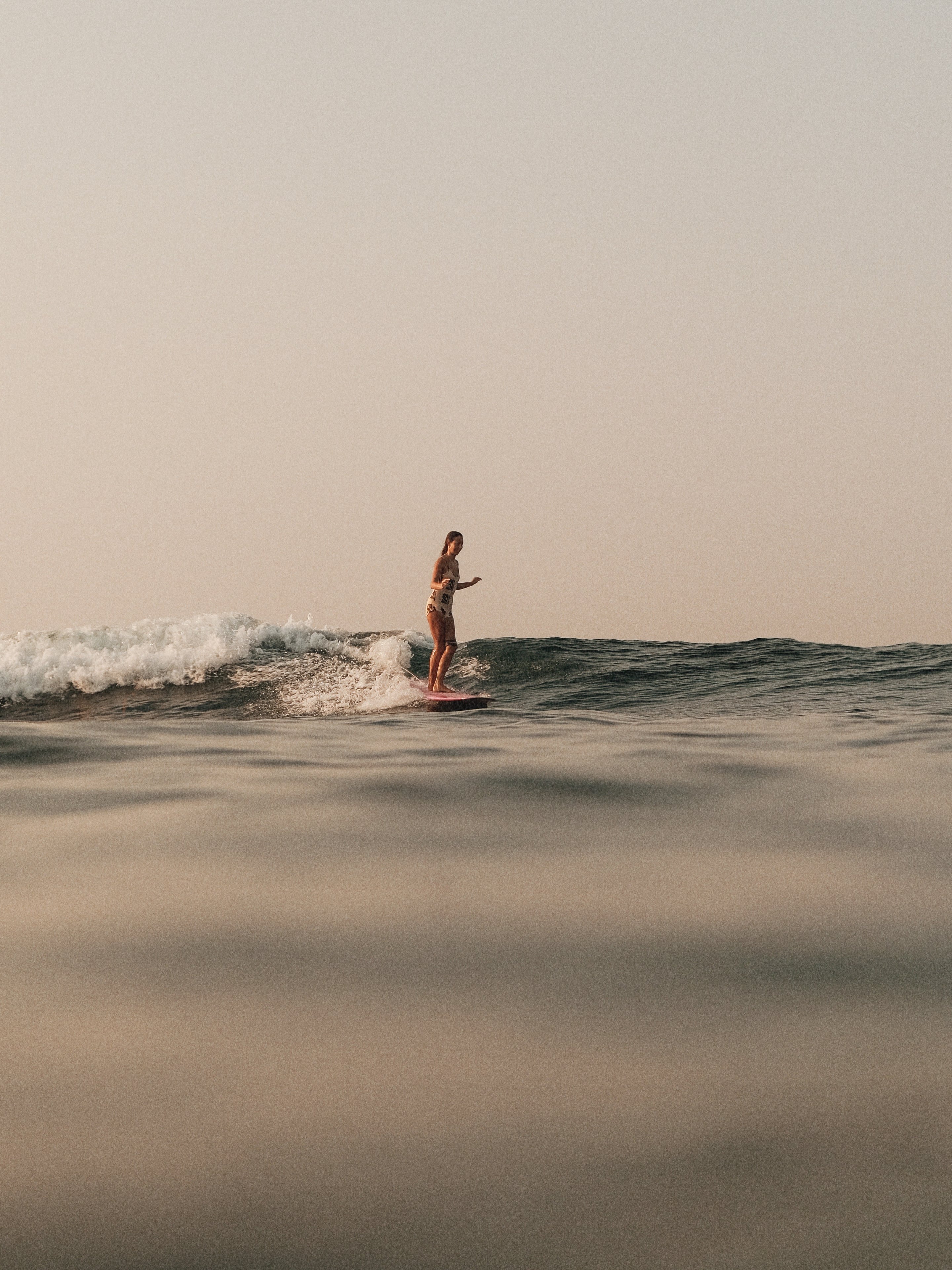 Frau steht auf einem Surfbrett und surft auf einer Welle im Meer während des Sonnenuntergangs.