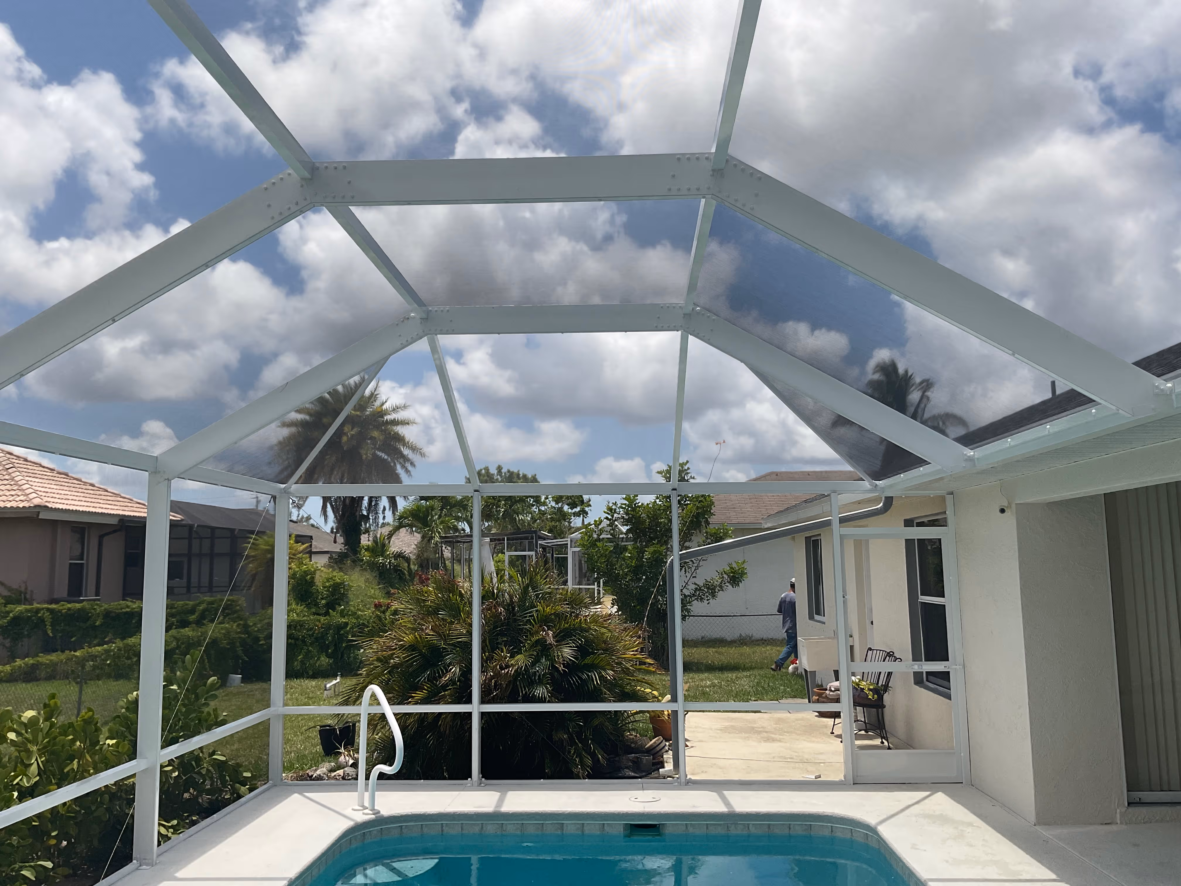 Interior view of white aluminum pool screen enclosure showing blue pool with screened roof and South Florida residential neighborhood beyond — AB Aluminum & Screens
