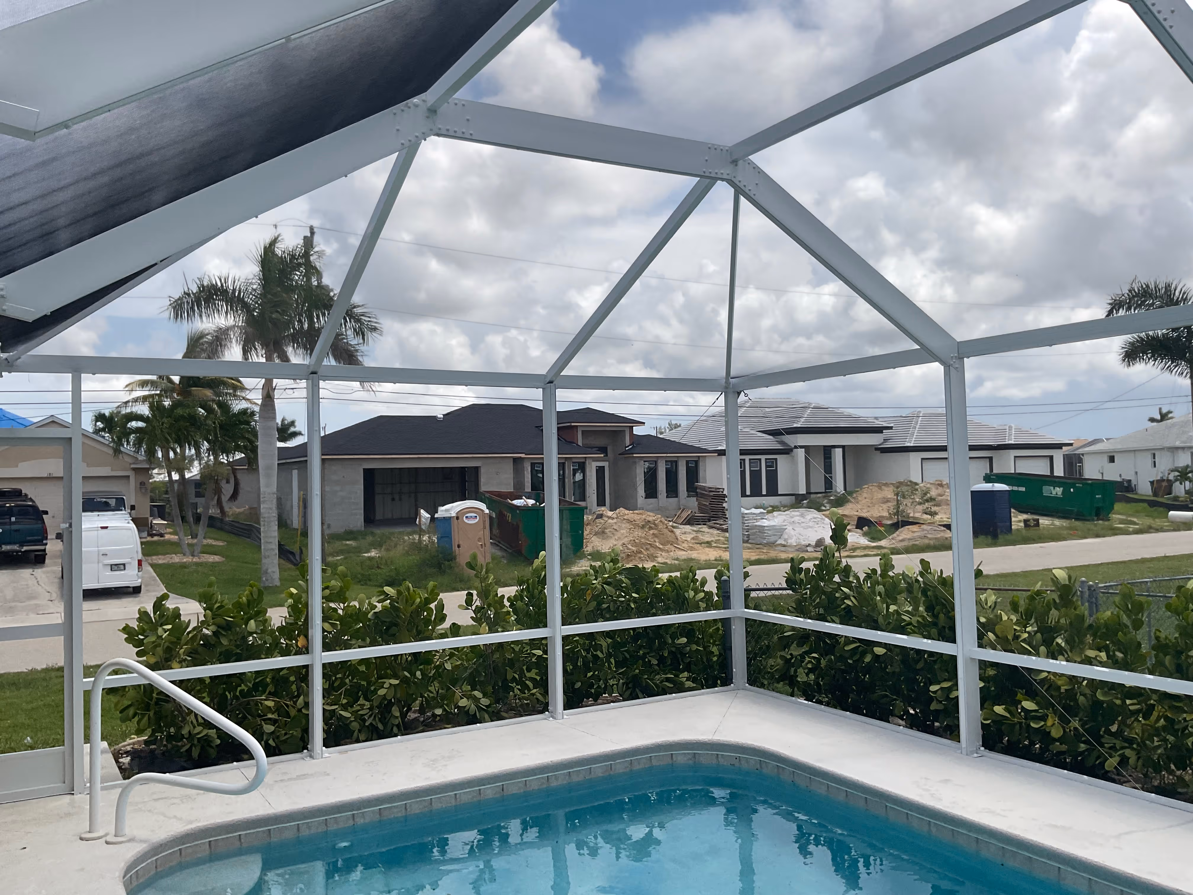 Interior of white aluminum pool enclosure with blue swimming pool, residential neighborhood with new homes and palm trees visible — AB Aluminum & Screens