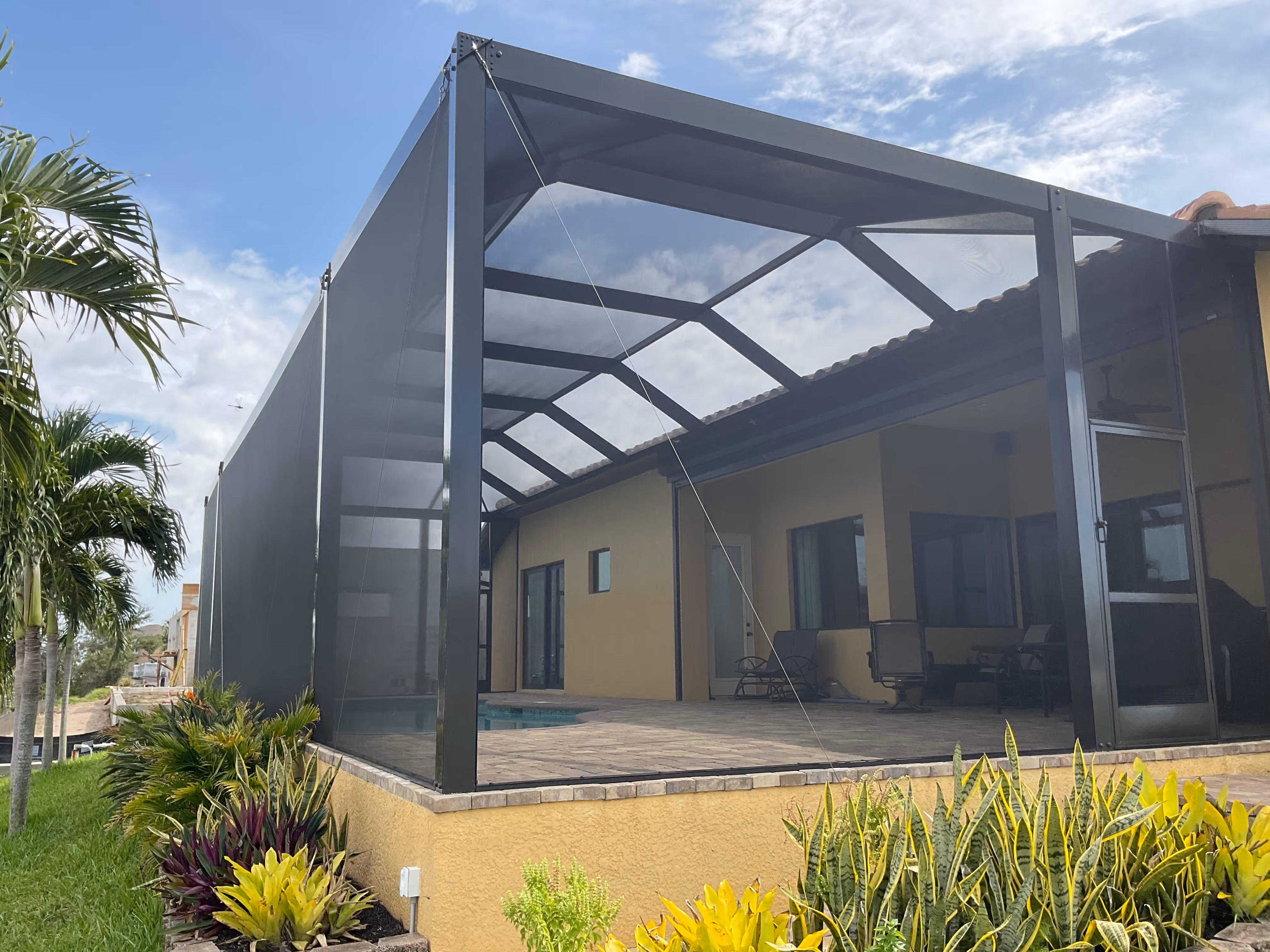 Exterior view of bronze aluminum pool screen enclosure attached to luxury South Florida home with tropical landscaping and palm trees — AB Aluminum & Screens