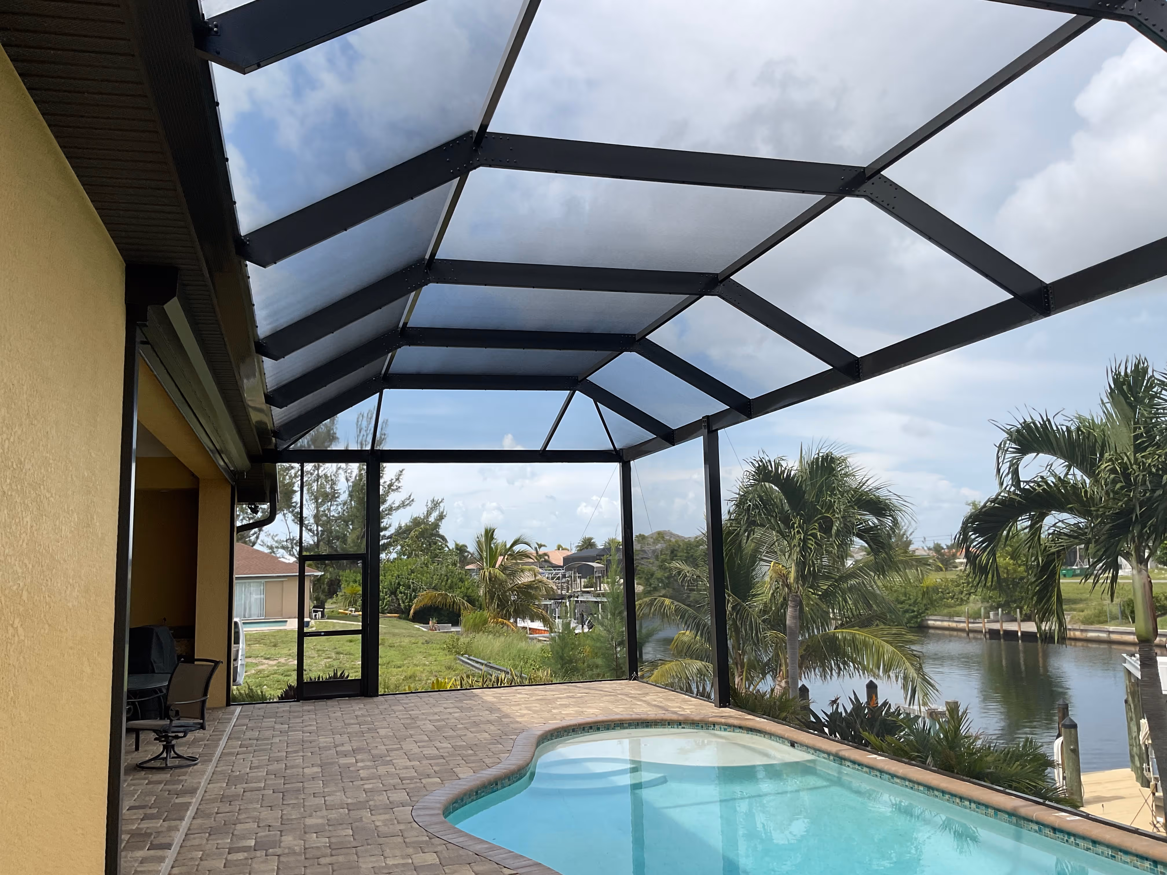 Interior of dark bronze aluminum pool screen enclosure with kidney-shaped pool overlooking waterfront canal with palm trees and private dock — AB Aluminum & Screens