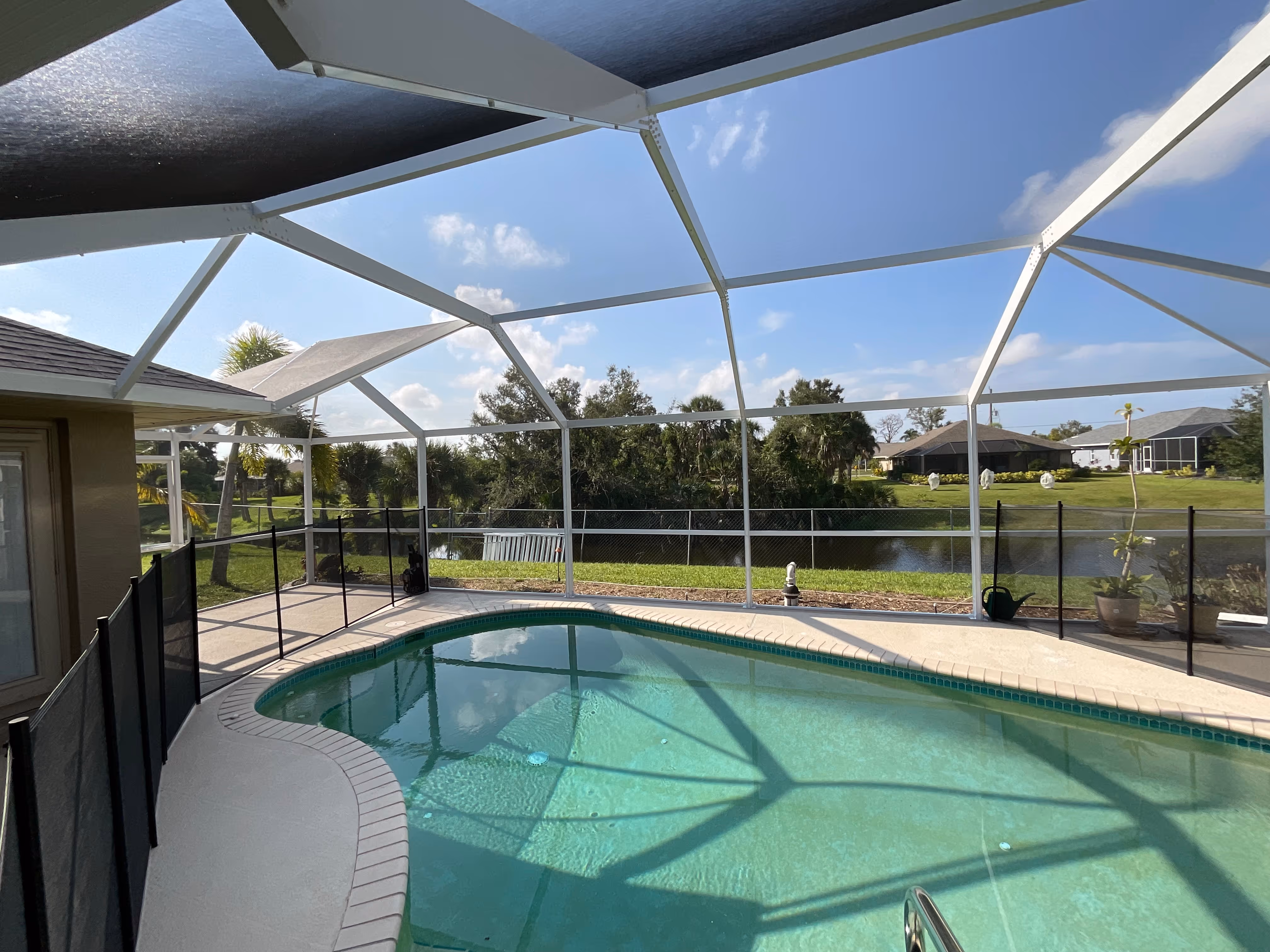 White aluminum pool screen enclosure interior with curved pool, paver deck, lake view and lush South Florida landscaping — AB Aluminum & Screens