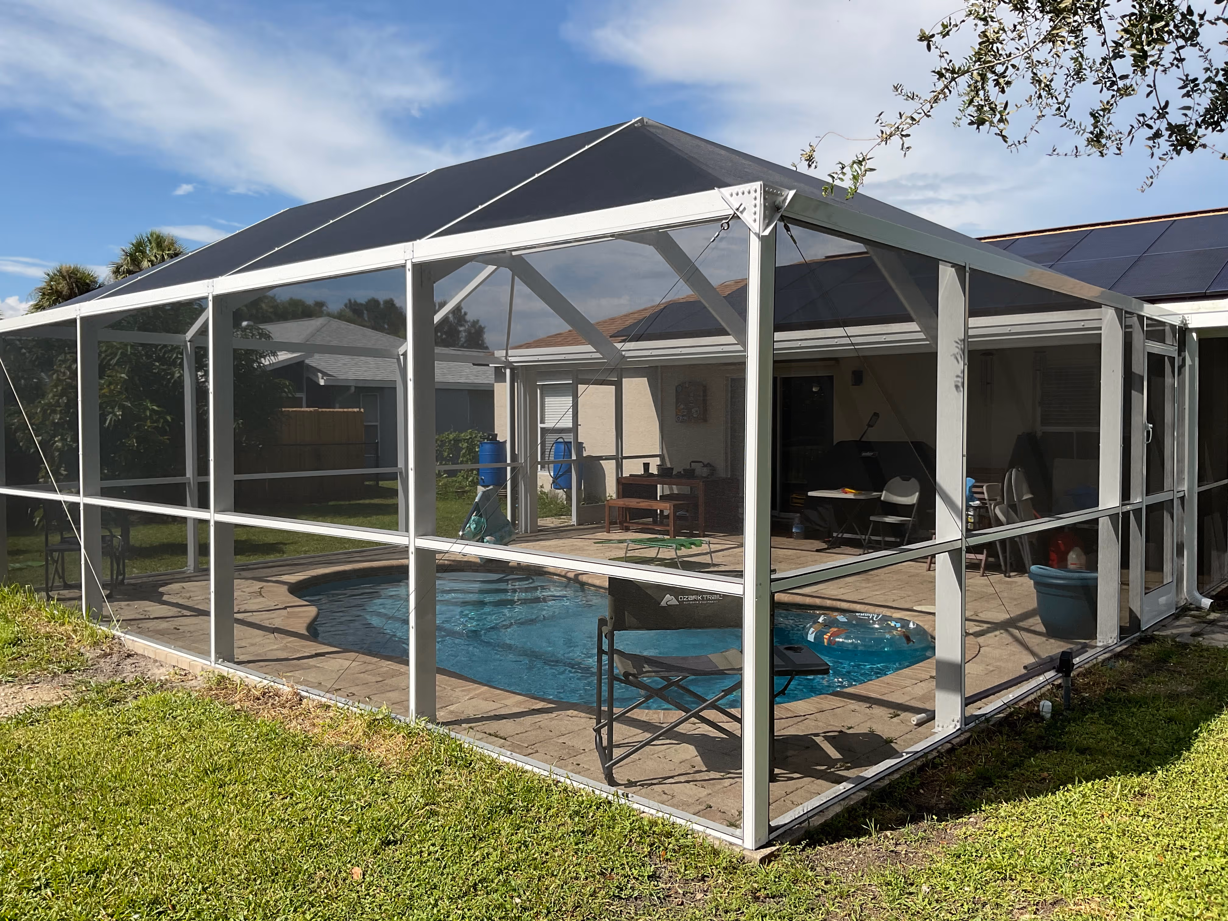 White aluminum pool screen enclosure interior with curved pool overlooking peaceful lake and green lawn, South Florida residential property — AB Aluminum & Screens