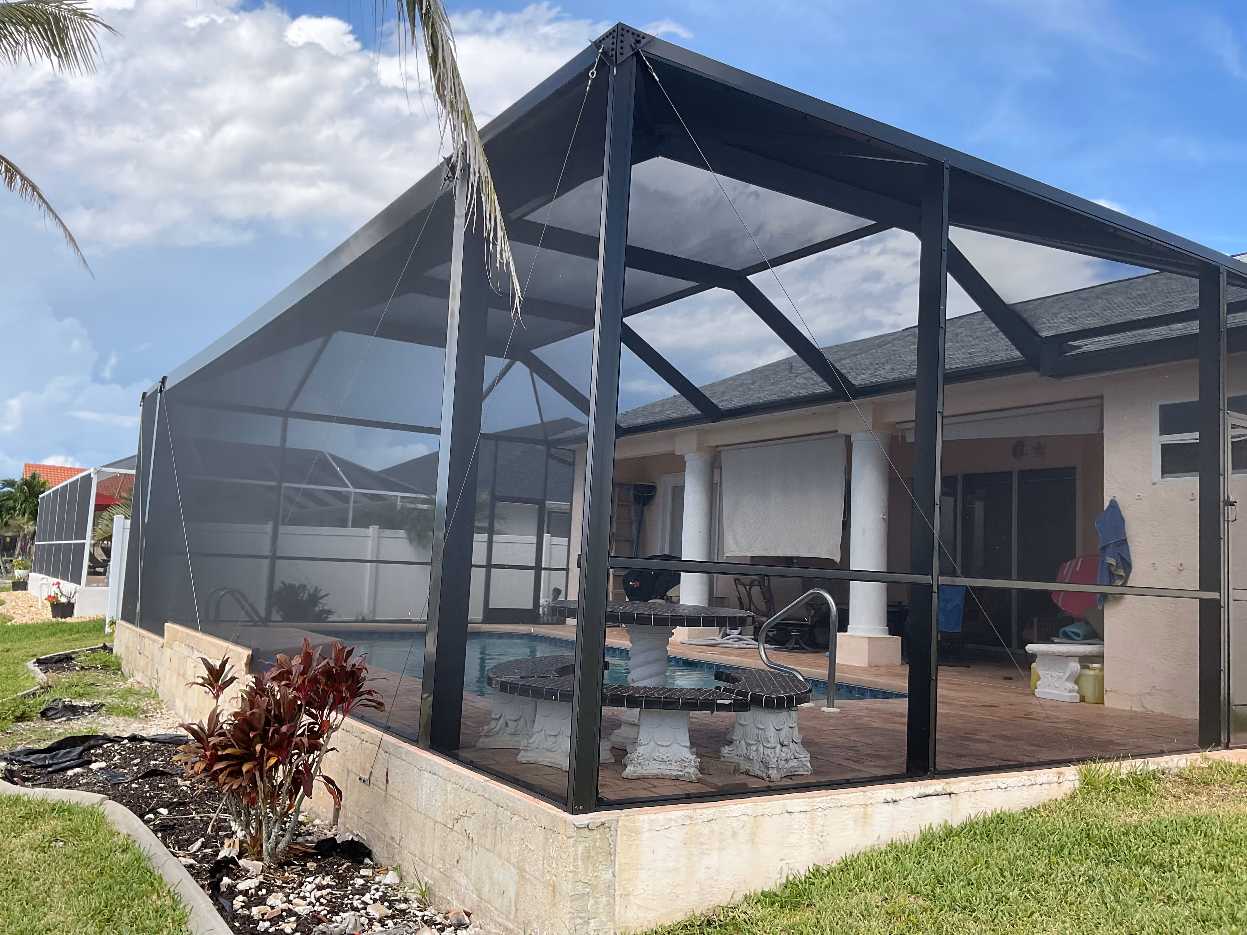 Dark bronze aluminum pool screen enclosure interior, freeform pool with open water view beyond, South Florida residential backyard — AB Aluminum & Screens