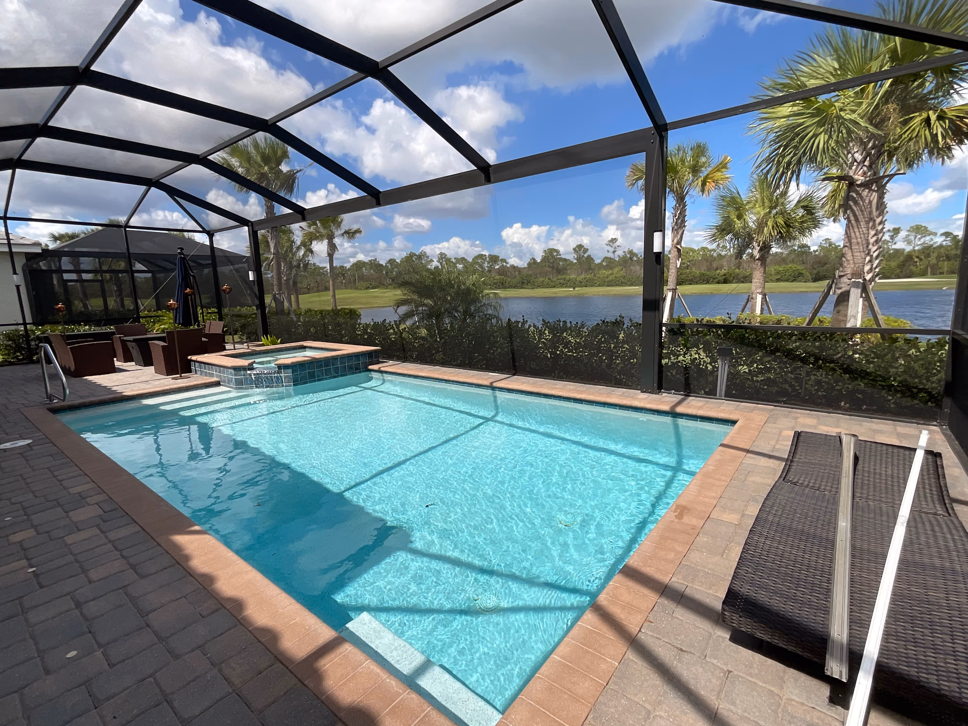 Dark bronze aluminum pool enclosure, rectangular pool with elevated spa, marble paver deck and lake view with palm trees, South Florida — AB Aluminum & Screens