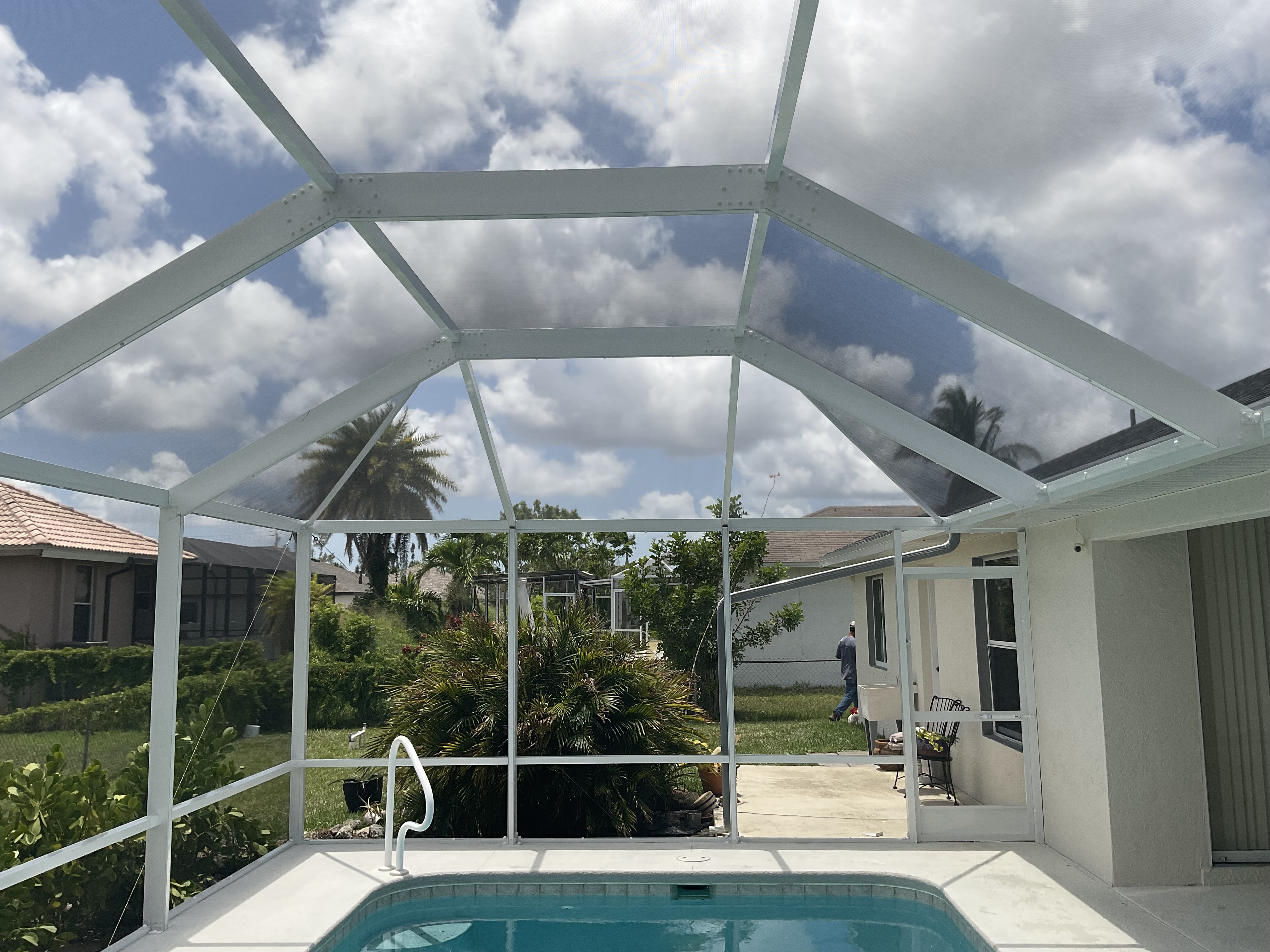 Interior view of white aluminum pool screen enclosure showing blue pool with screened roof and South Florida residential neighborhood beyond — AB Aluminum & Screens