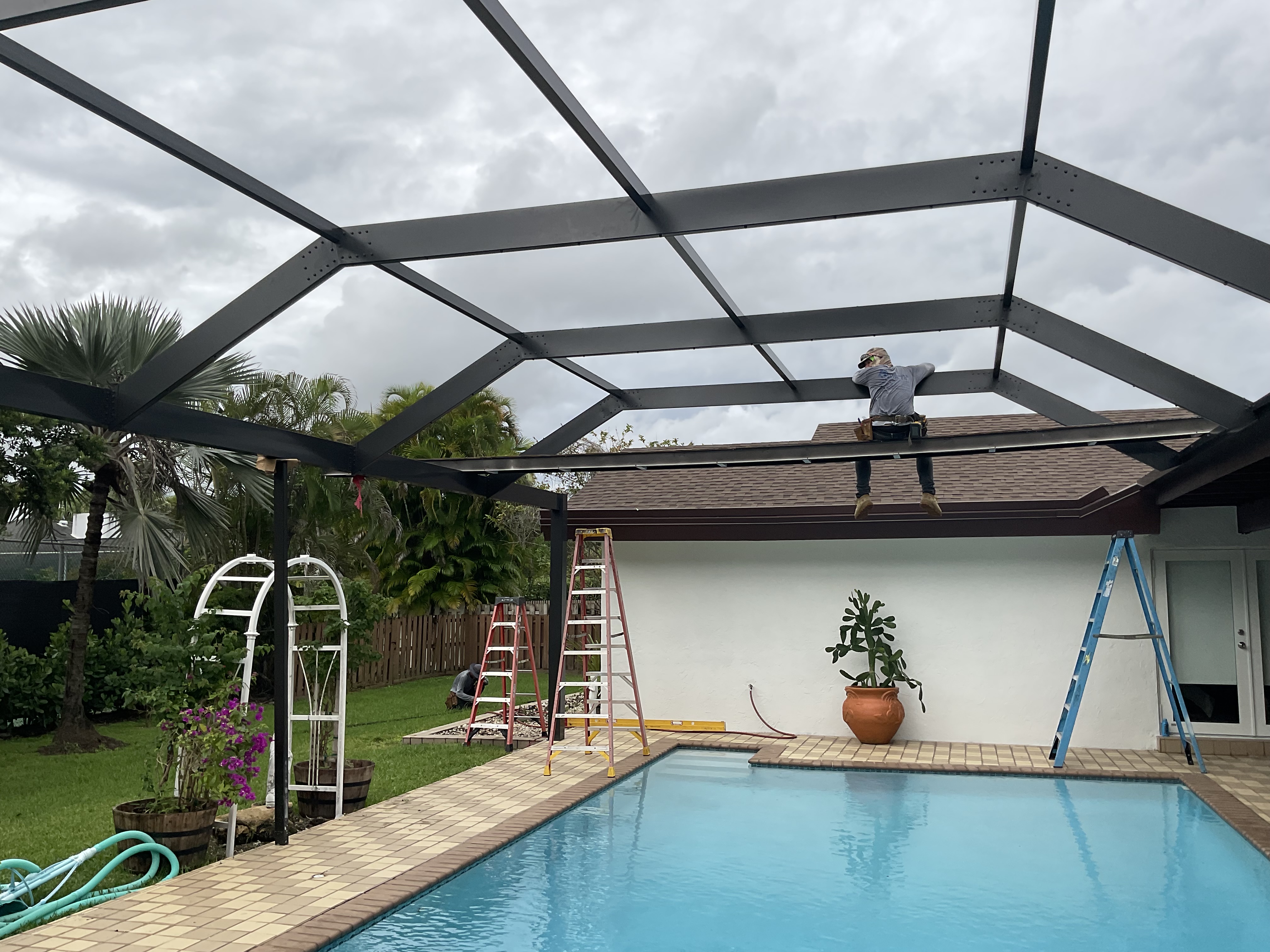 Dark bronze aluminum pool enclosure gable roof interior, freeform pool with concrete paver deck, South Florida backyard — AB Aluminum & Screens