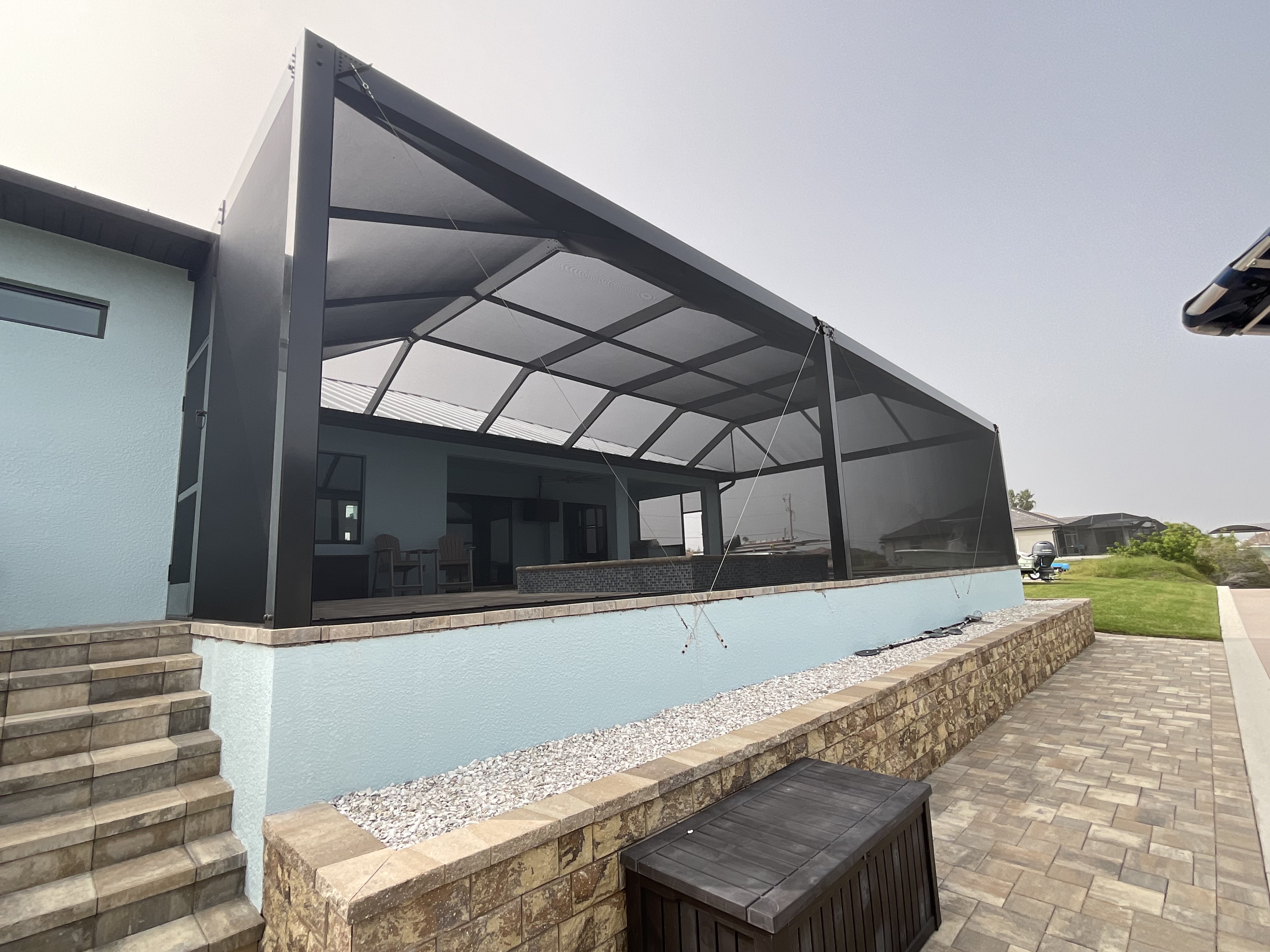 Dark charcoal aluminum pool screen enclosure lean-to roof, exterior view on modern light-blue stucco home with paver steps, South Florida — AB Aluminum & Screens