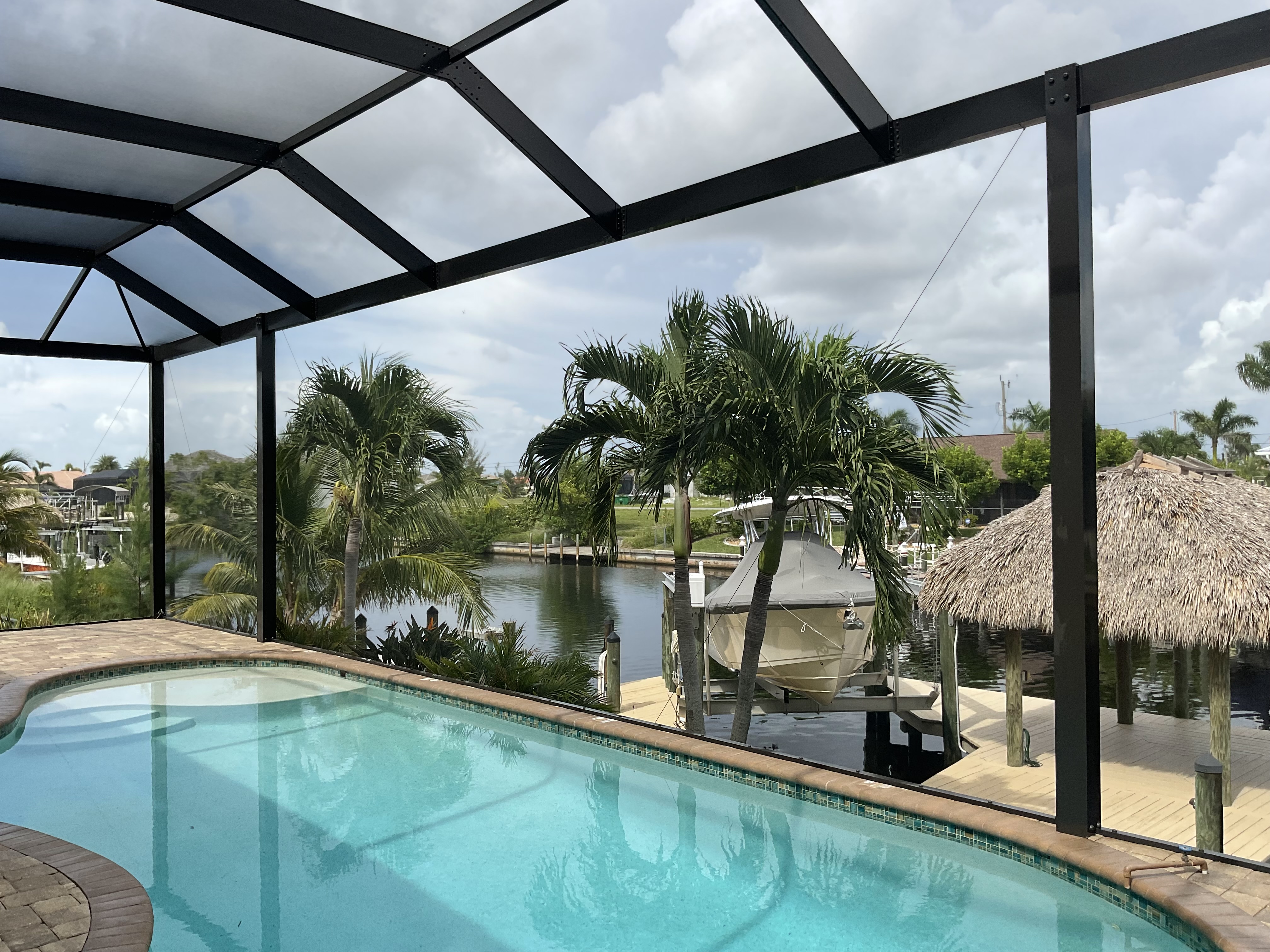 Interior view of dark bronze pool enclosure with irregular-shaped pool, waterfront canal with private boat dock, tiki hut and palm trees — AB Aluminum & Screens