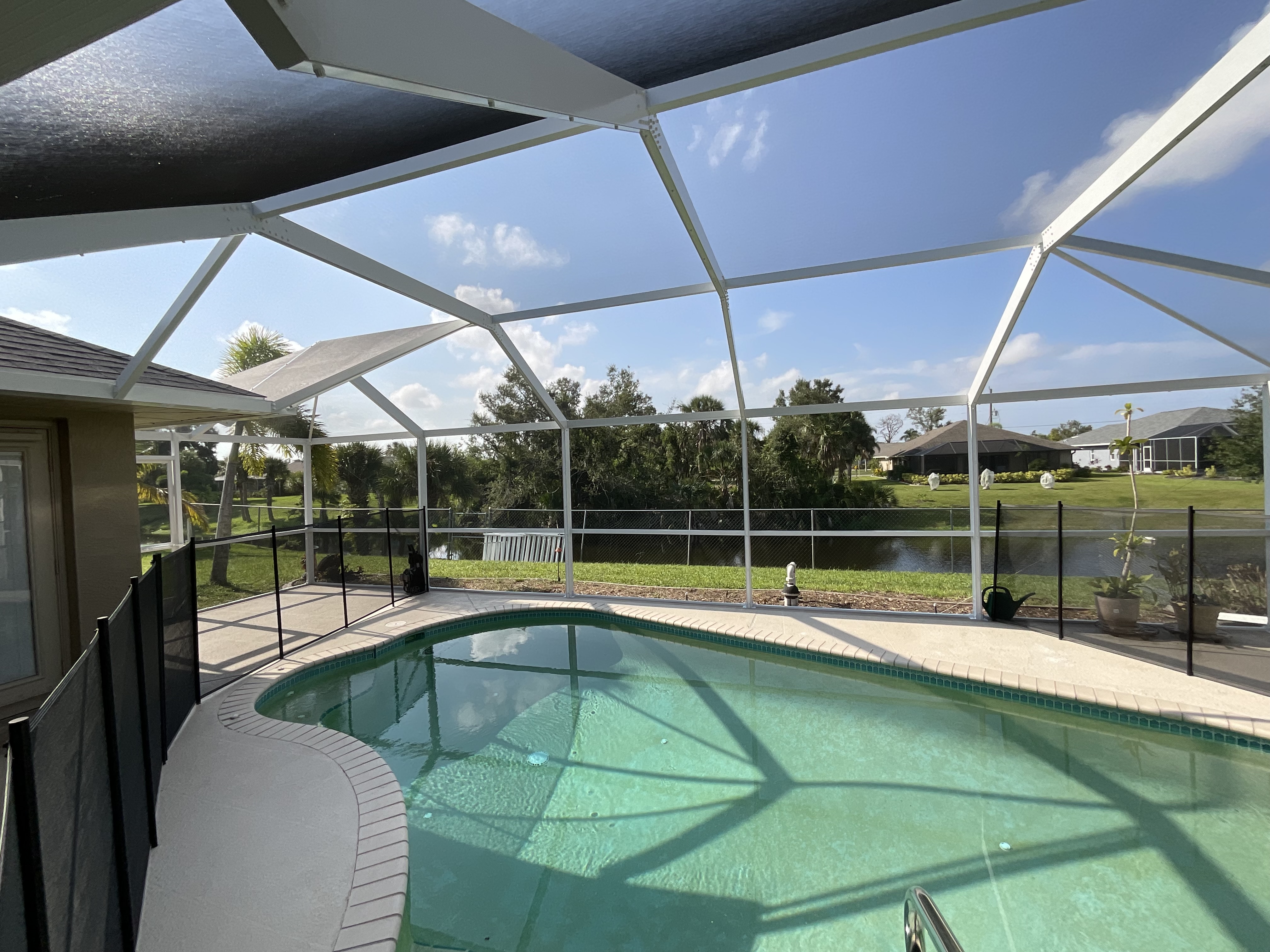 White aluminum pool screen enclosure interior with curved pool, paver deck, lake view and lush South Florida landscaping — AB Aluminum & Screens