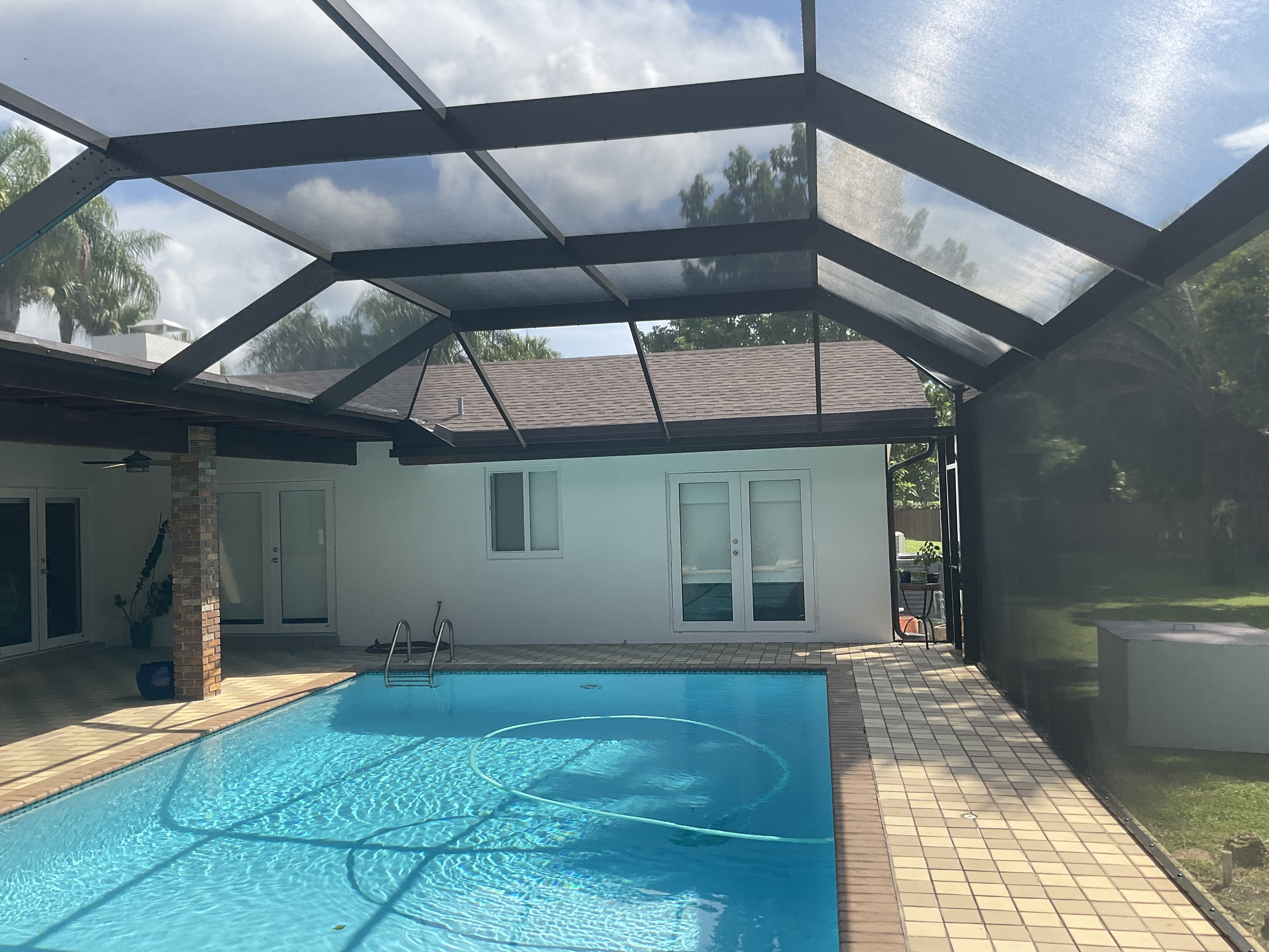 Dark bronze aluminum pool screen enclosure interior, rectangular pool with tile deck and French doors, stucco home, South Florida — AB Aluminum & Screens
