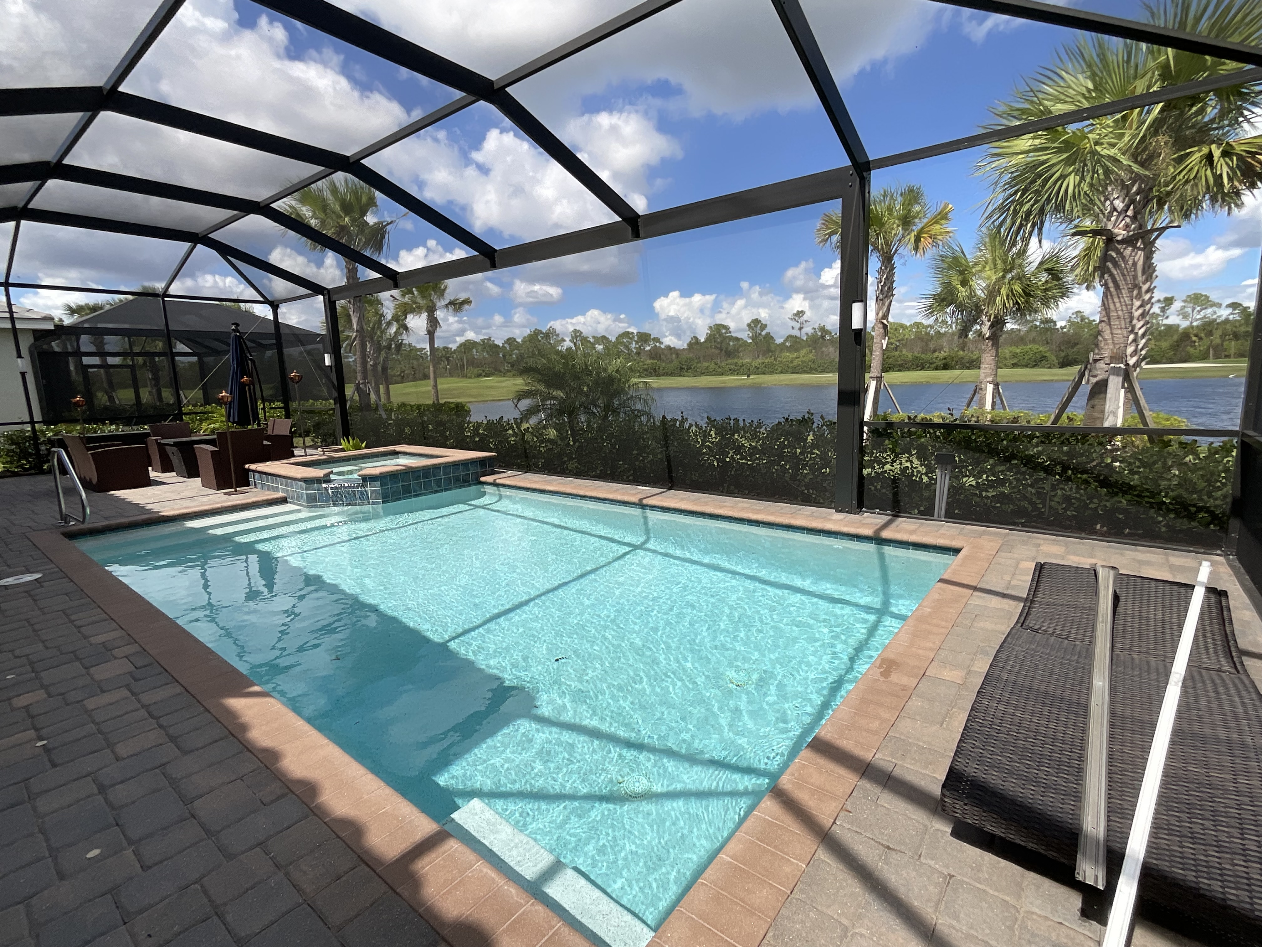 Dark bronze aluminum pool enclosure, rectangular pool with elevated spa, marble paver deck and lake view with palm trees, South Florida — AB Aluminum & Screens